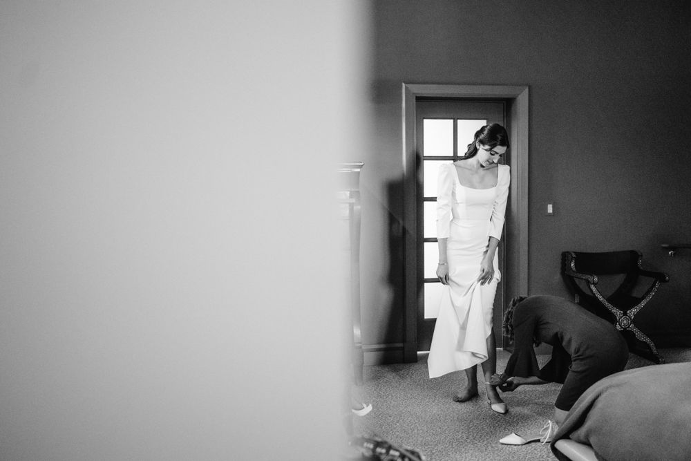 Black and white photo of someone in white attire standing in a doorway during preparations.