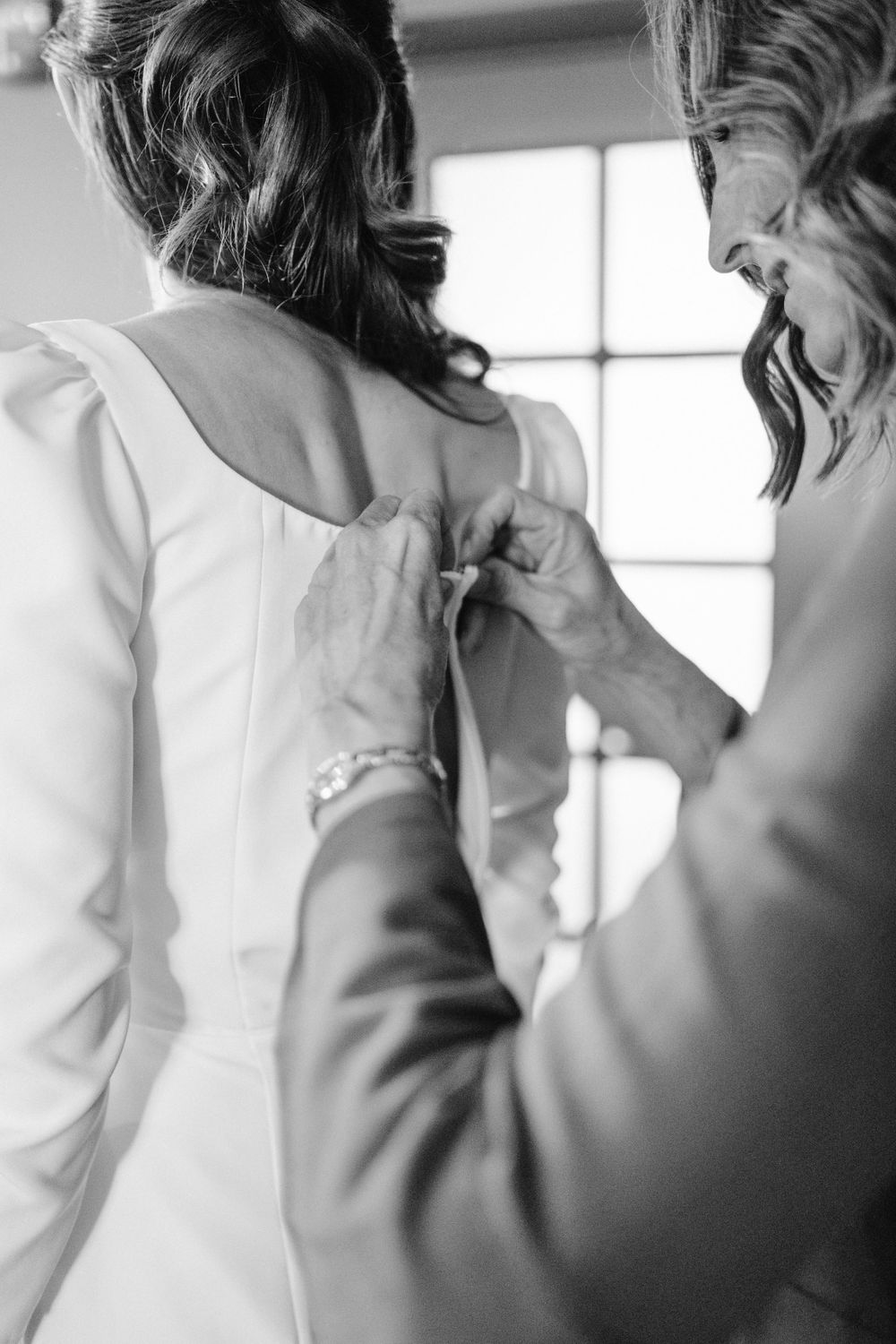 Close-up black and white shot of someone helping button up a formal white dress.