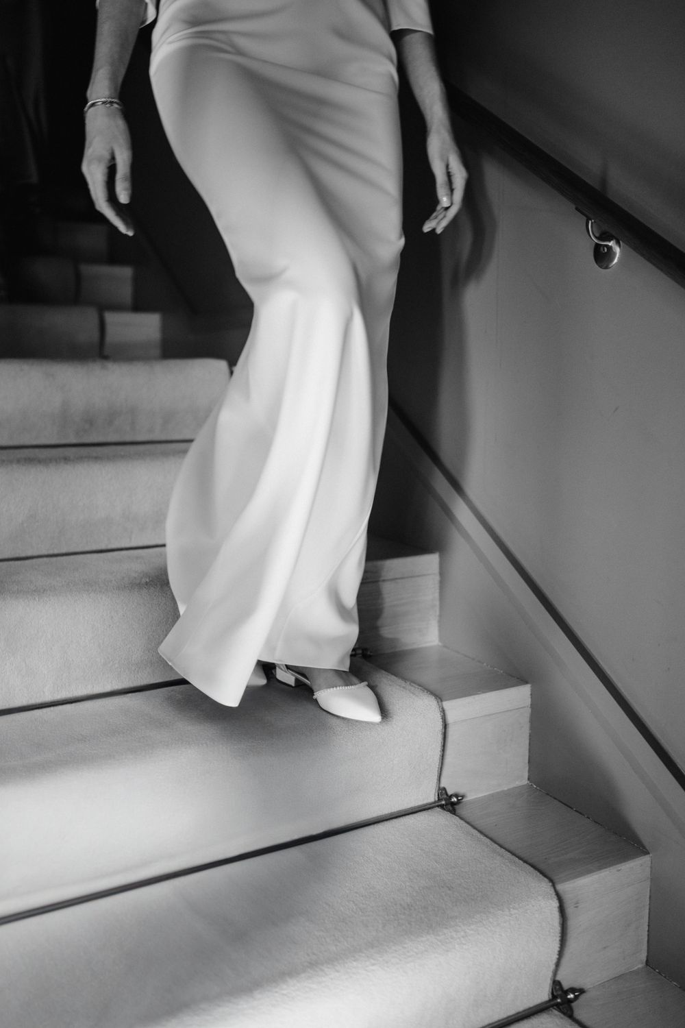 Close-up of an elegant white dress and shoes descending stairs.