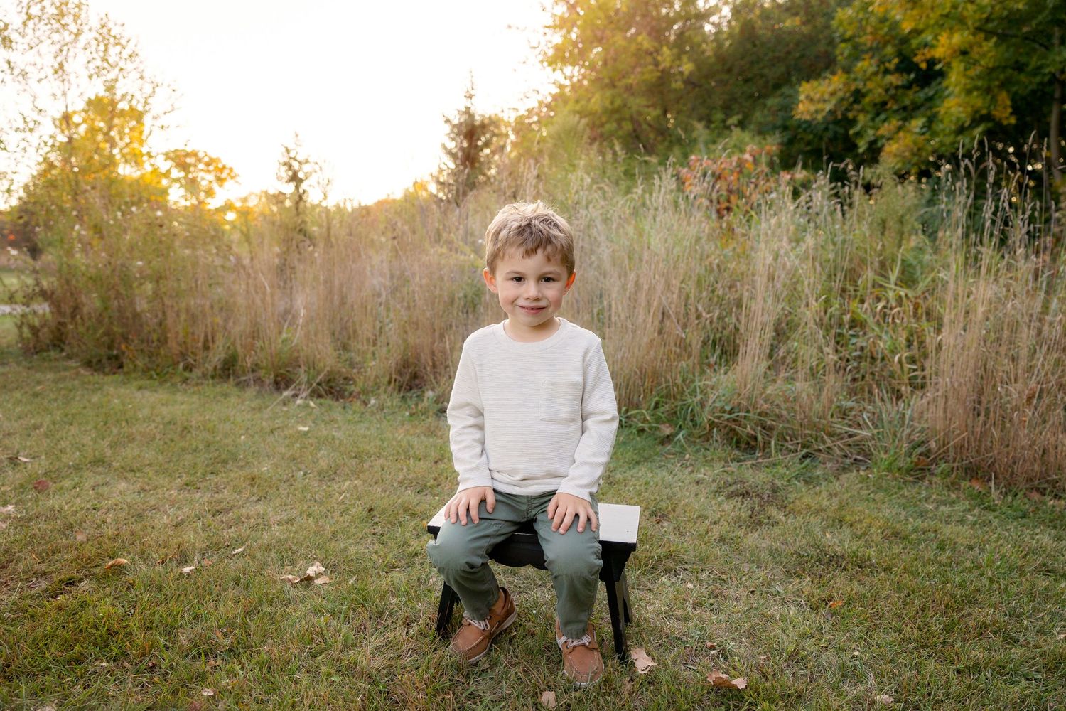 Child sitting on wooden bench outdoors during golden hour.