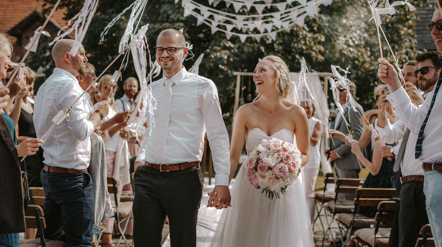 Happy wedding celebration with guests holding streamers as newlyweds walk down outdoor aisle.