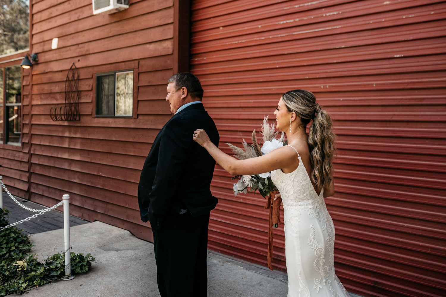 First look moment between bride and groom in front of rustic red barn wall.