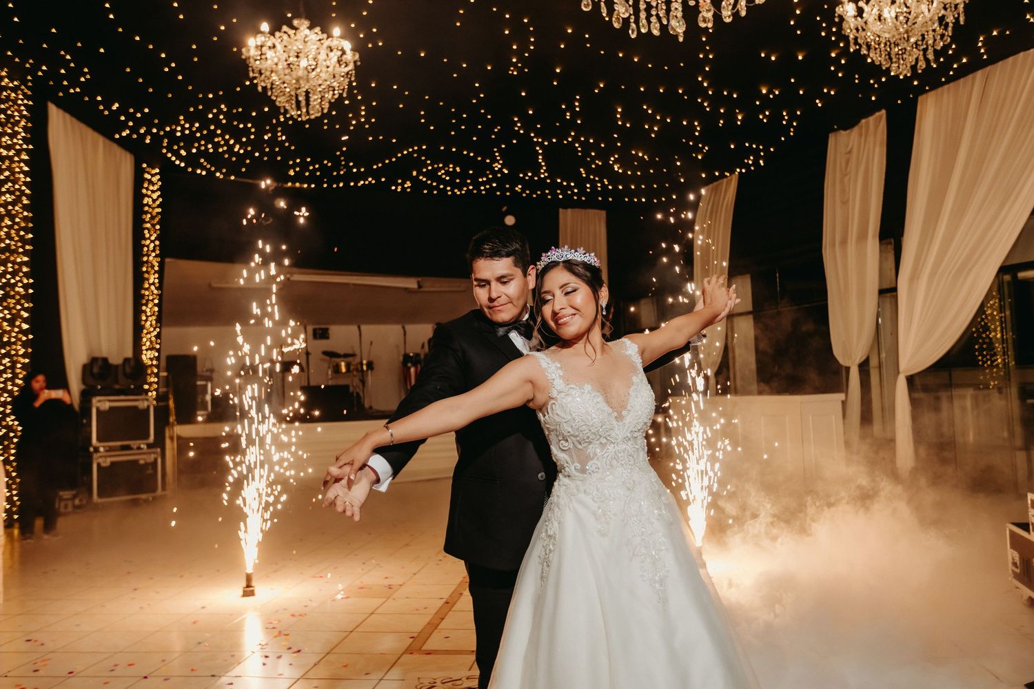 Newlyweds celebrating with sparklers on dance floor under crystal chandeliers and string lights.