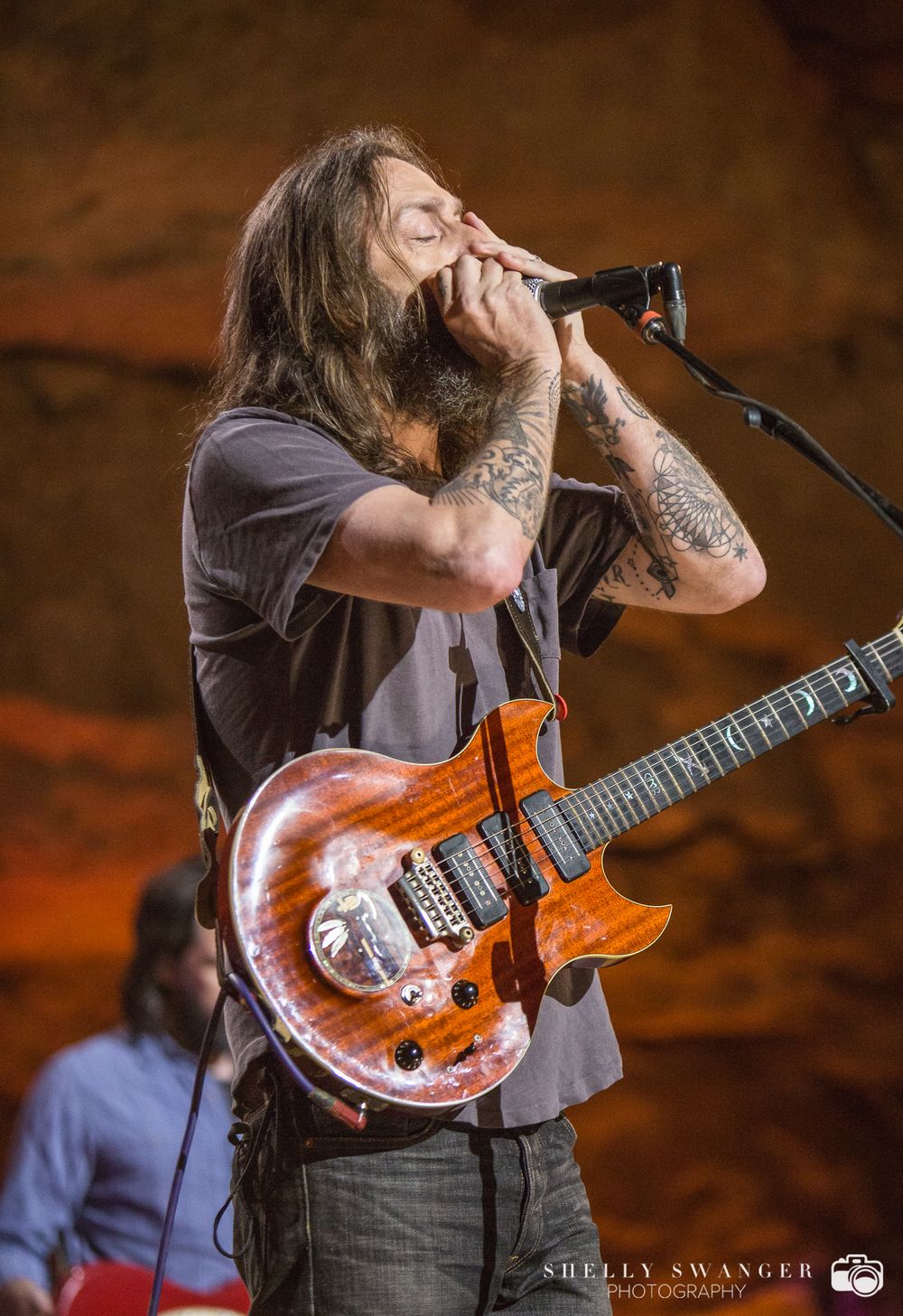 Chris Robinson performs with an orange electric guitar on stage.