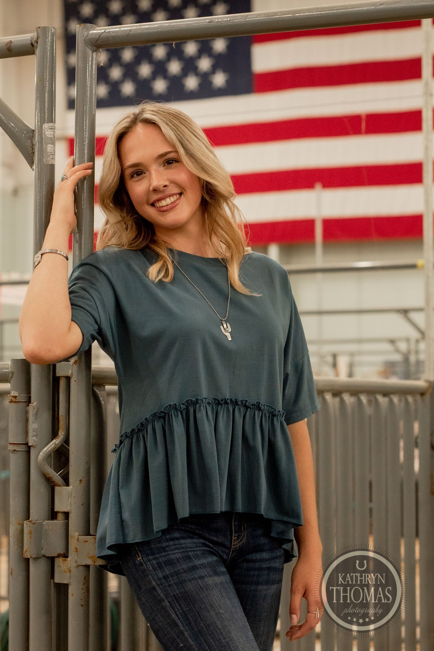 Close-up portrait with American flag backdrop highlights teal peplum top and casual style.