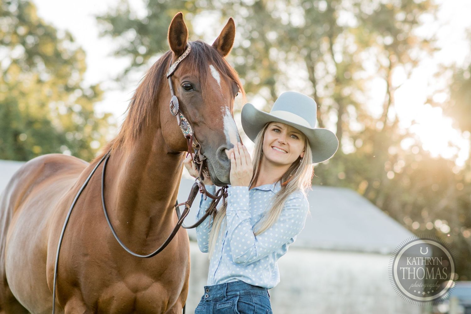 A sunlit portrait of a brown horse and its handler against a white barn backdrop.