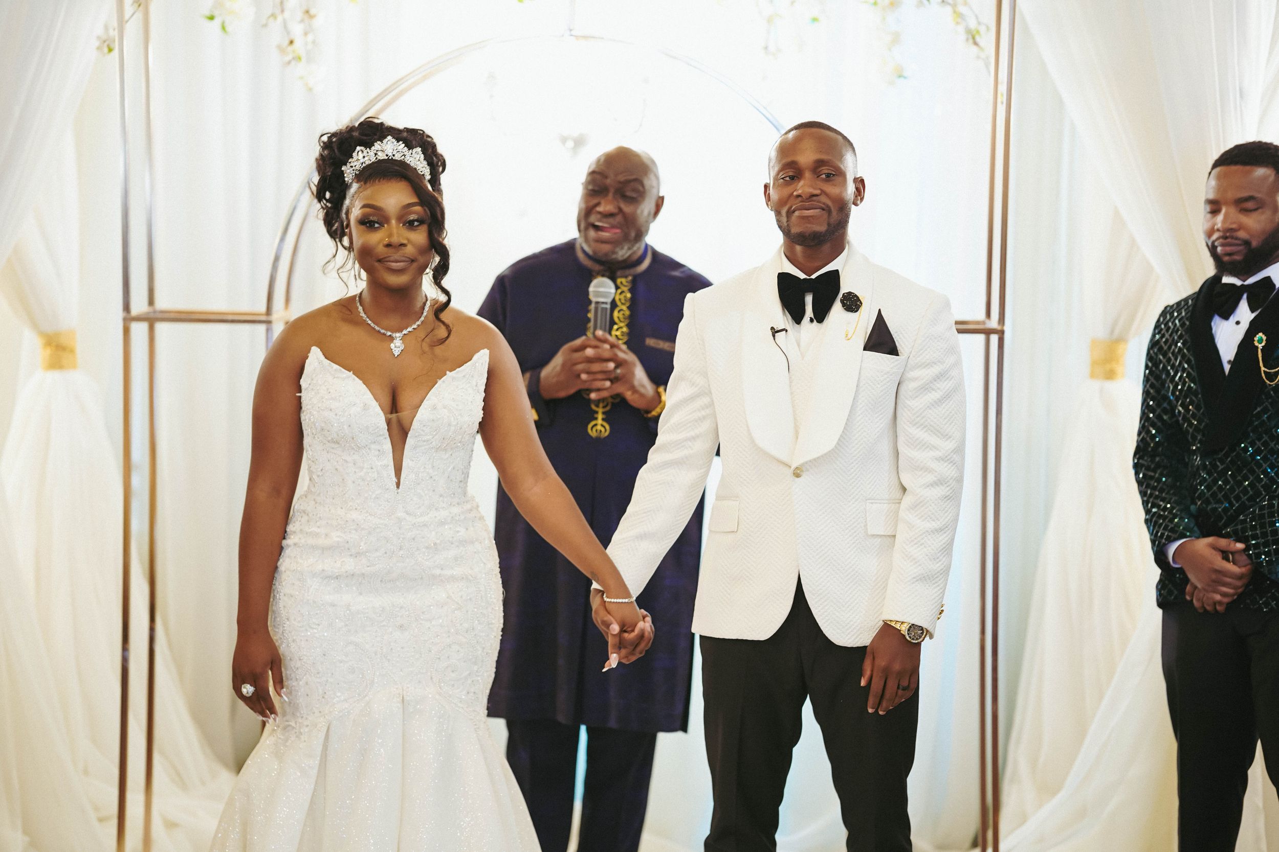 Wedding party celebrating with joy under a decorated white arch with golden accents.