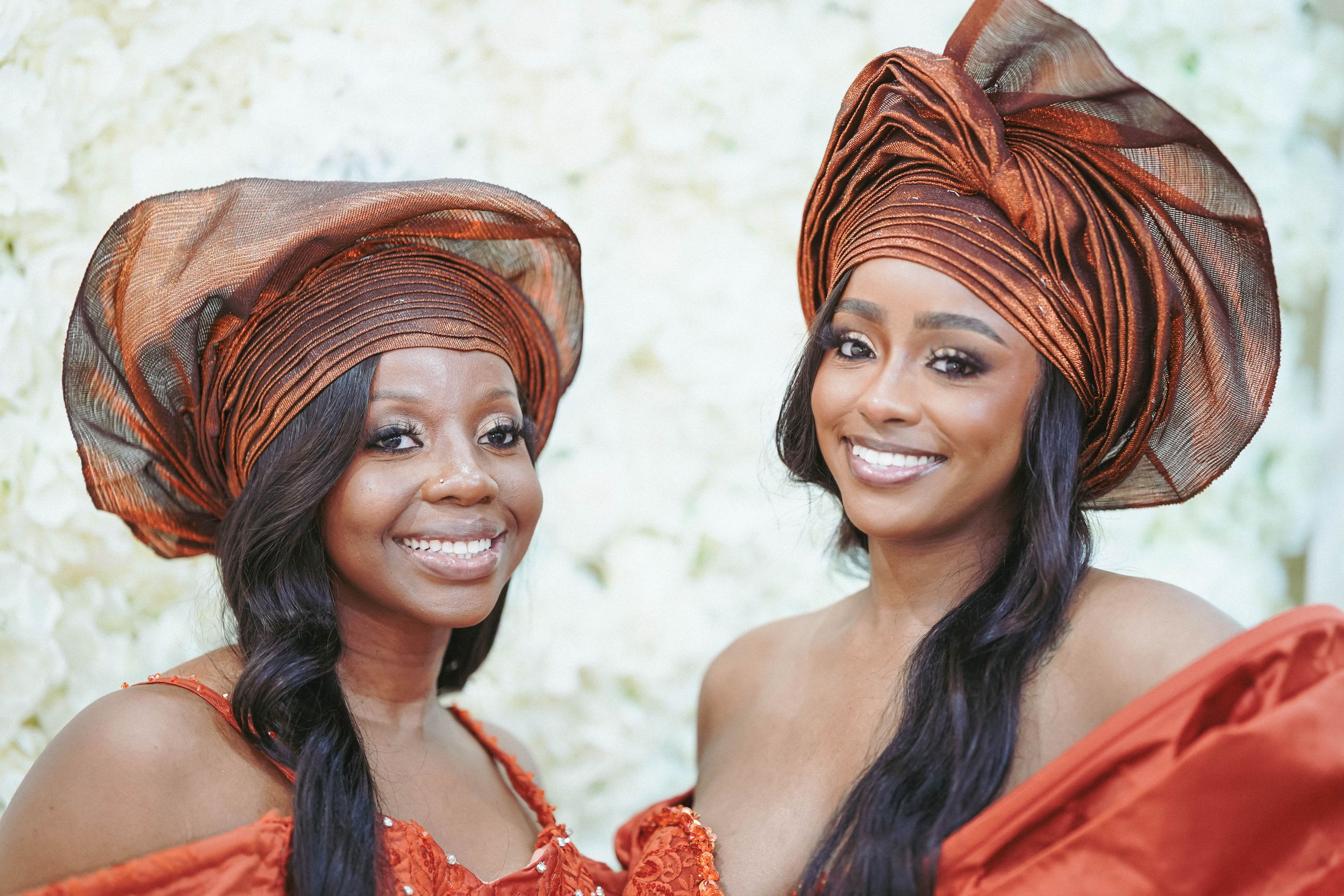 Women in ornate red attire and matching headwraps laugh and celebrate together.