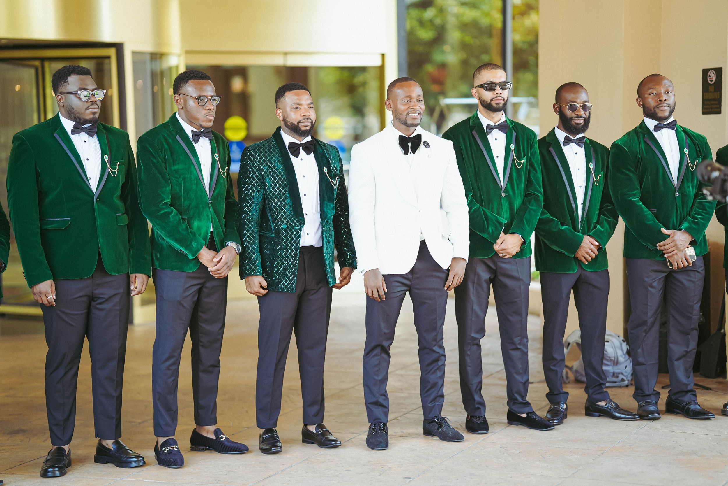 Groomsmen line up wearing coordinated emerald green jackets with black bow ties and white dress shirts.