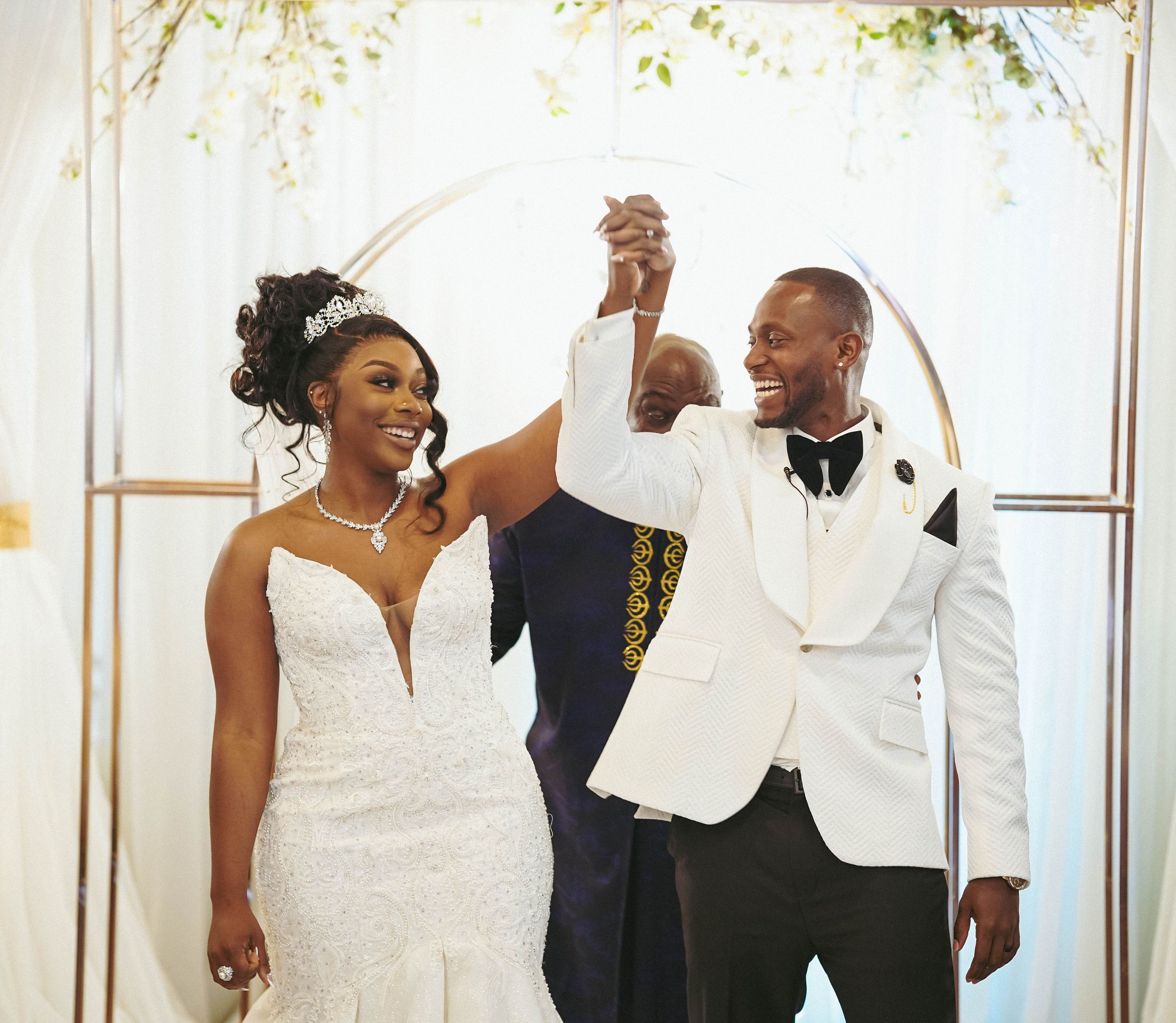 Formal wedding party gathering under an elegant white floral arch for celebration photos.