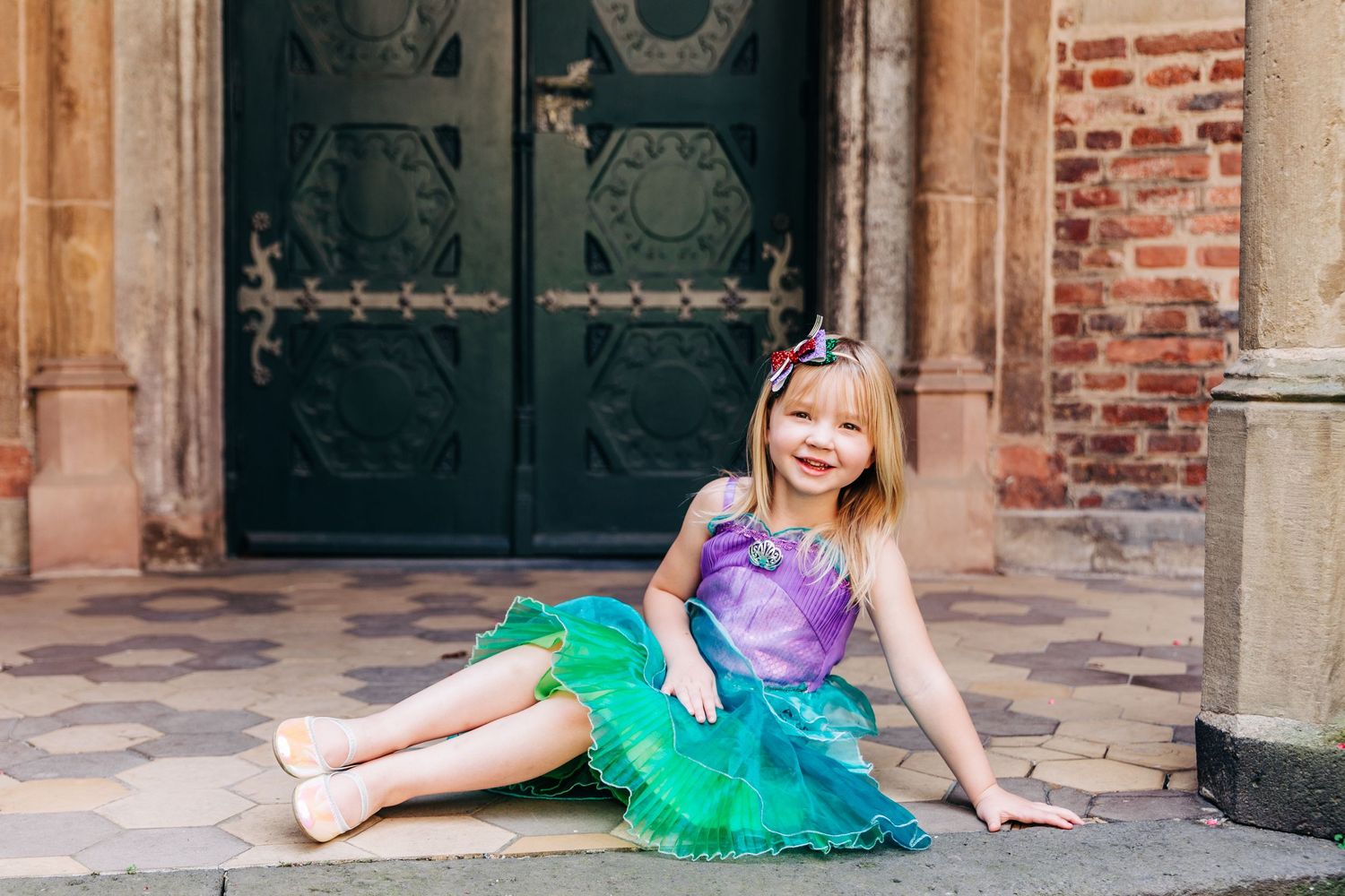 A princess-themed photo shoot against an ornate dark door and brick wall backdrop.