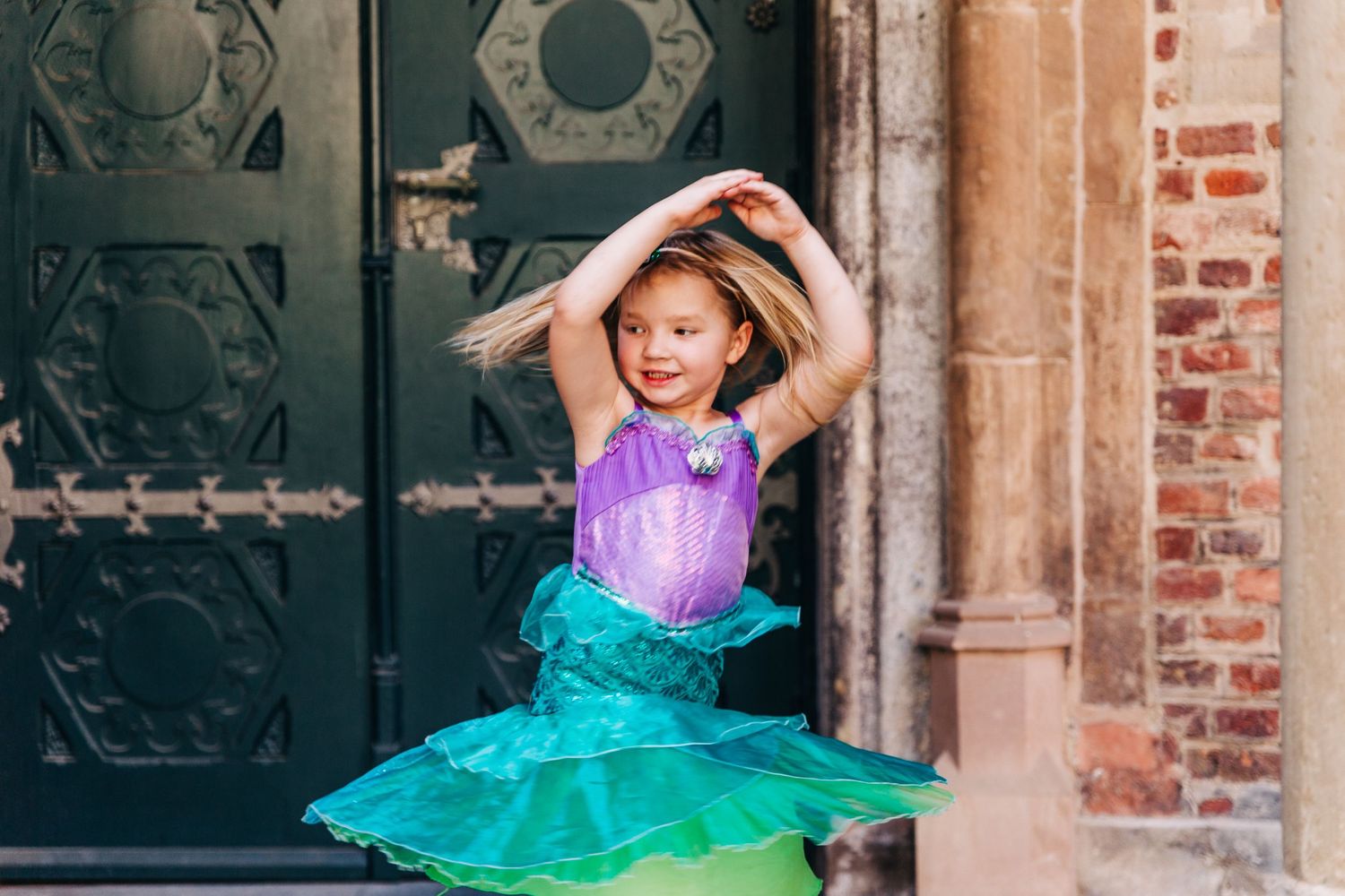 A cheerful dance pose in a purple and turquoise costume against a Gothic doorway.