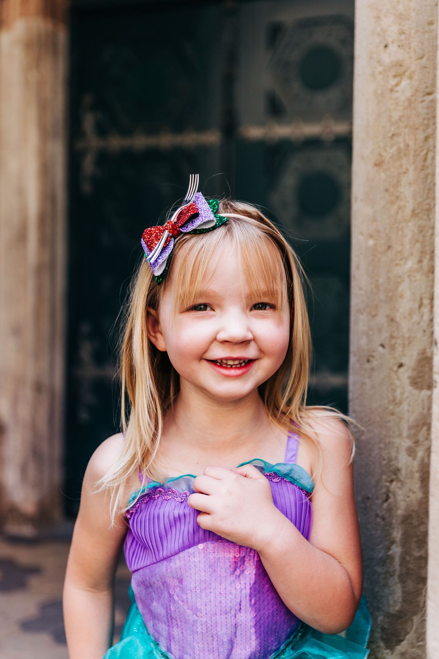 A bright smile captured in purple and turquoise costume against vintage architecture.