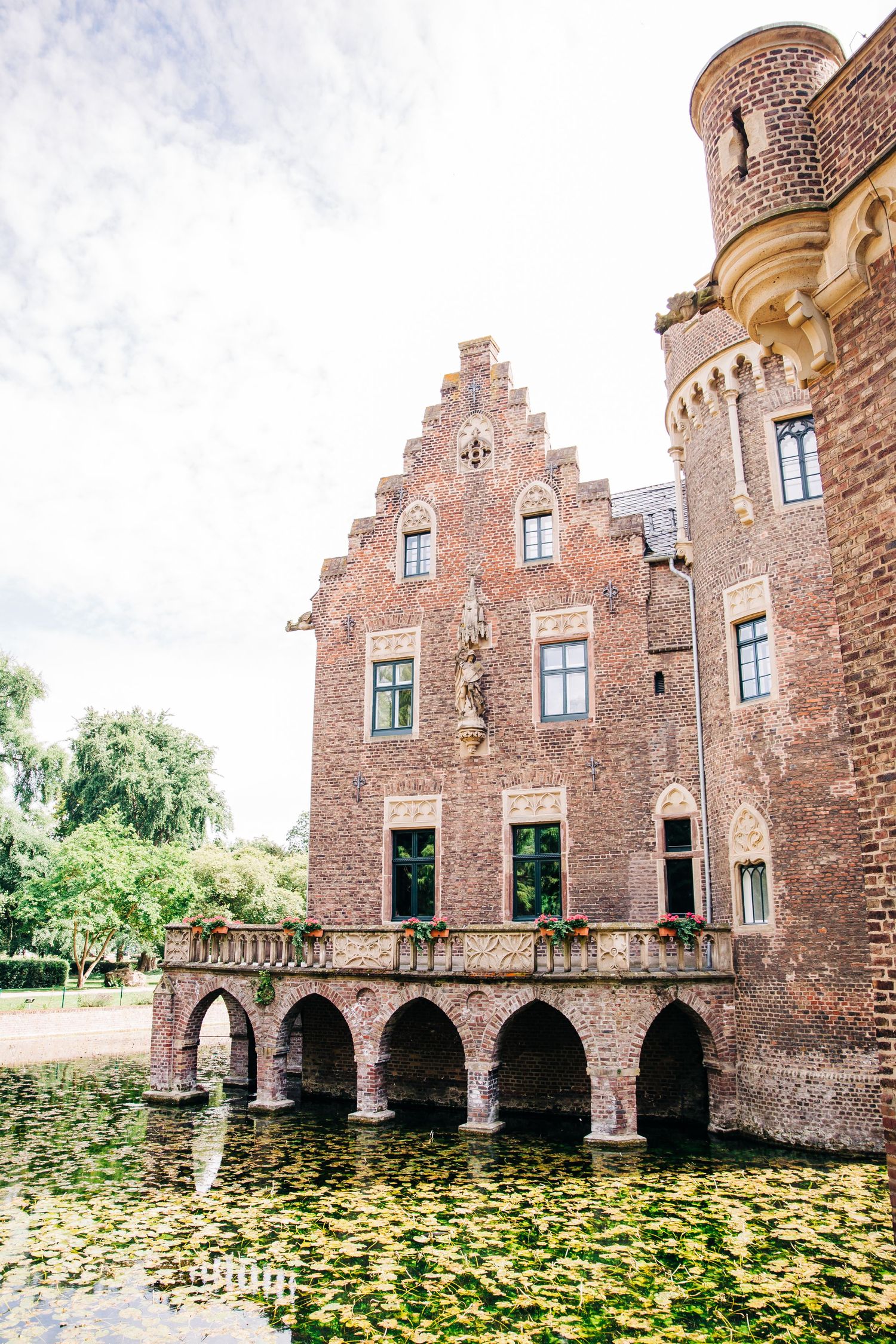 Ancient brick castle with arched bridge over lily pond reflecting in still water.