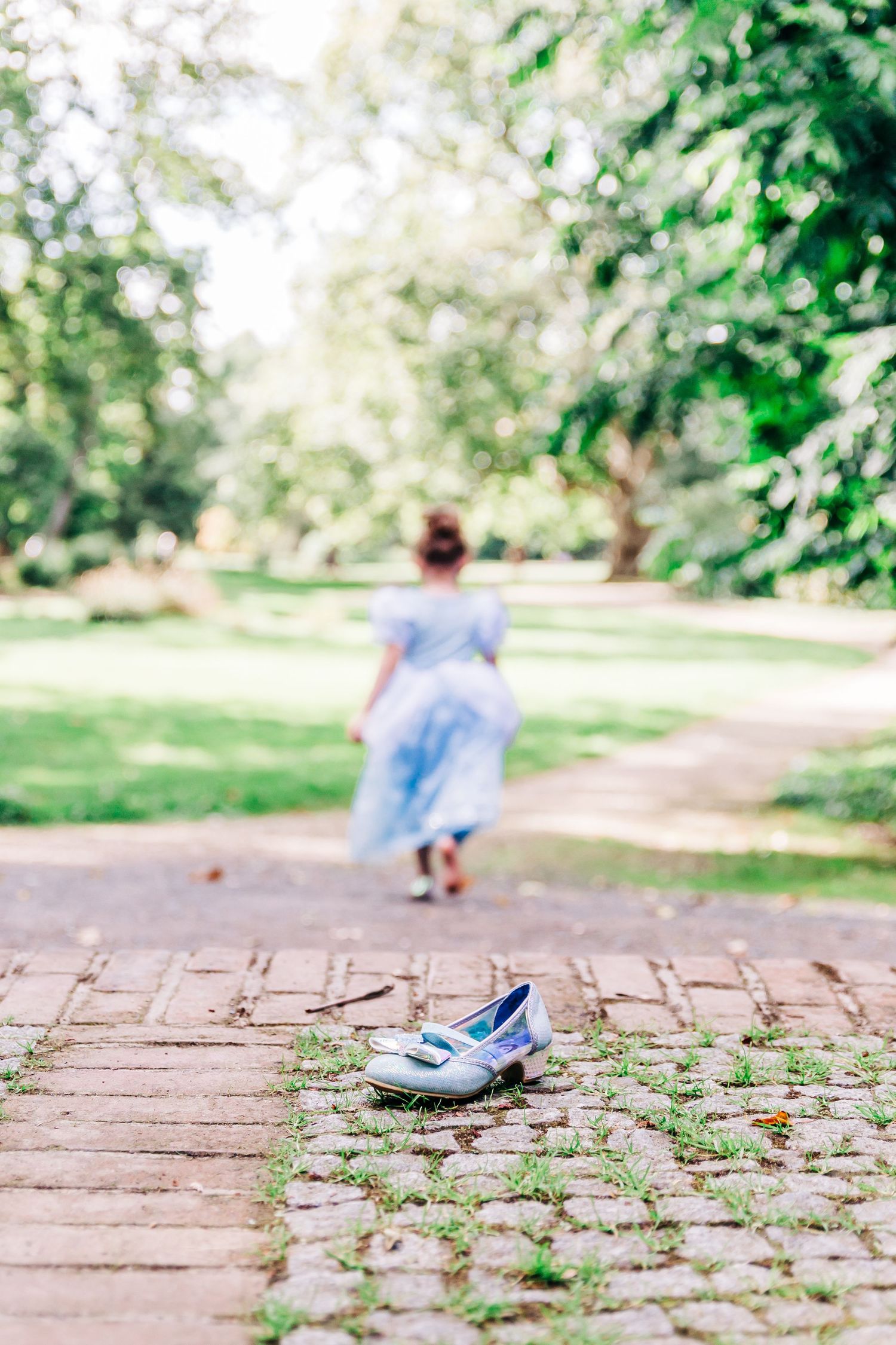 Lost glass slipper on brick path with blurred figure in blue dress walking away.