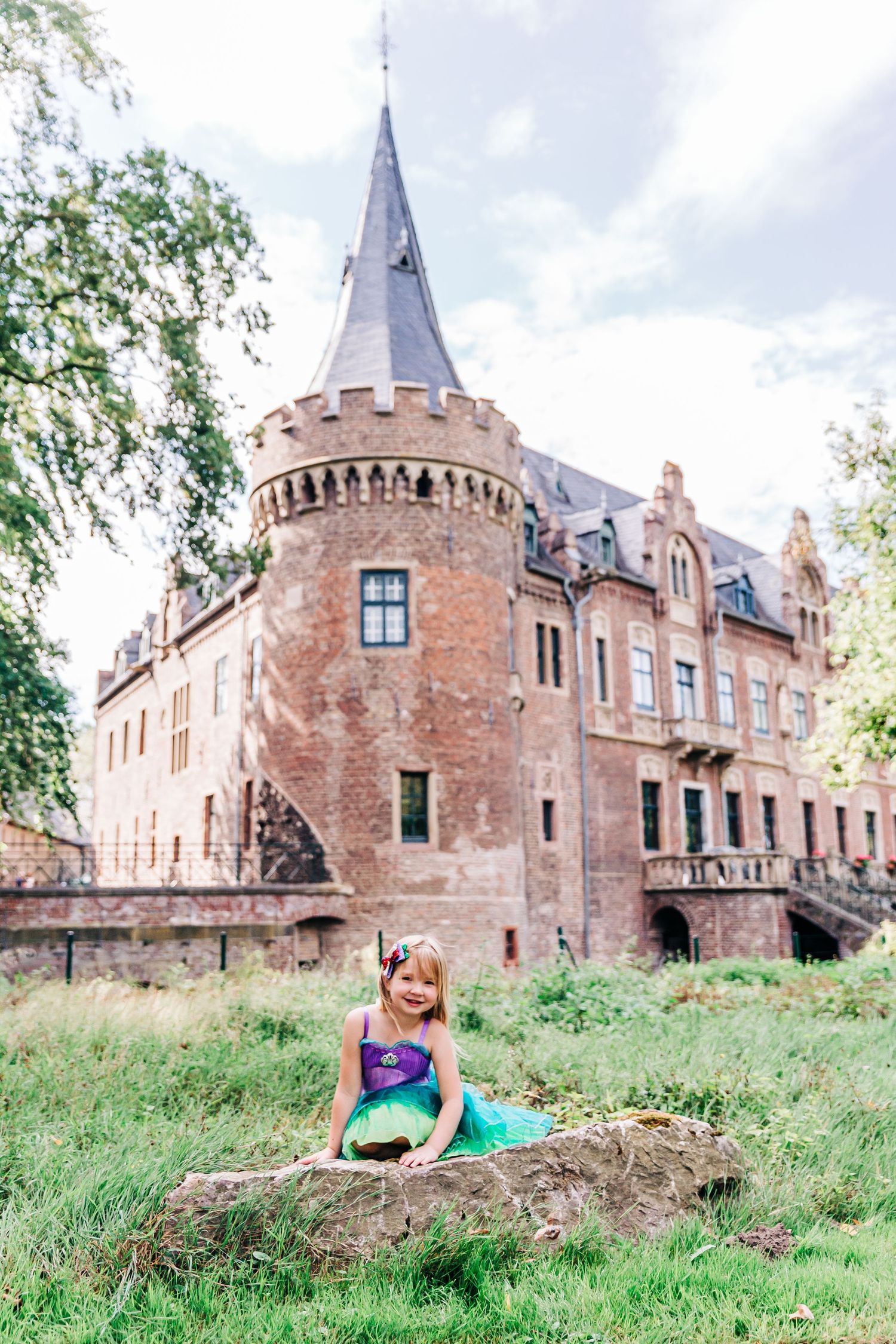A princess in green sits by a historic castle with turrets and stone walls.