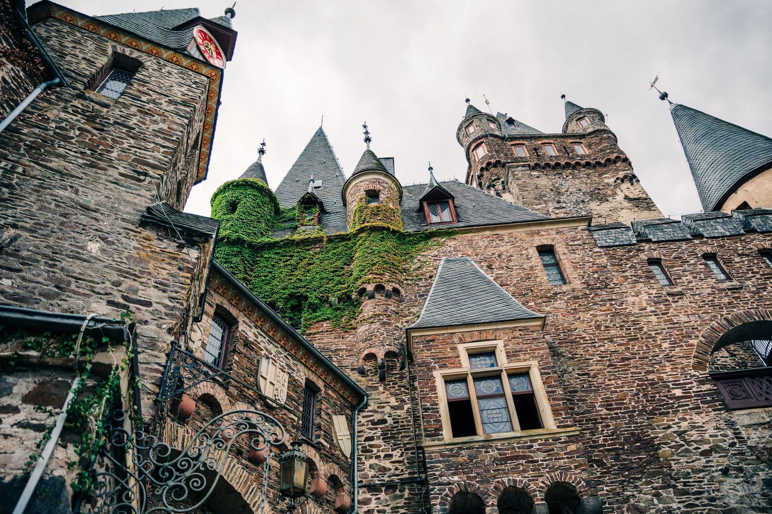 Medieval stone castle architecture with ivy-covered walls and Gothic spires against cloudy sky.