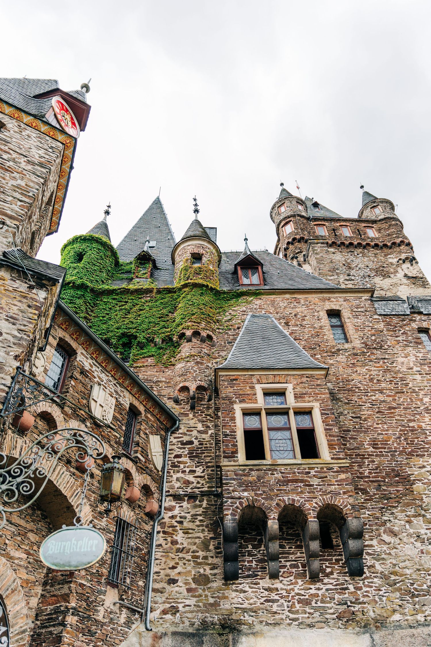 Historic castle facade with ivy-covered stone walls, Gothic architecture and multiple spired towers.