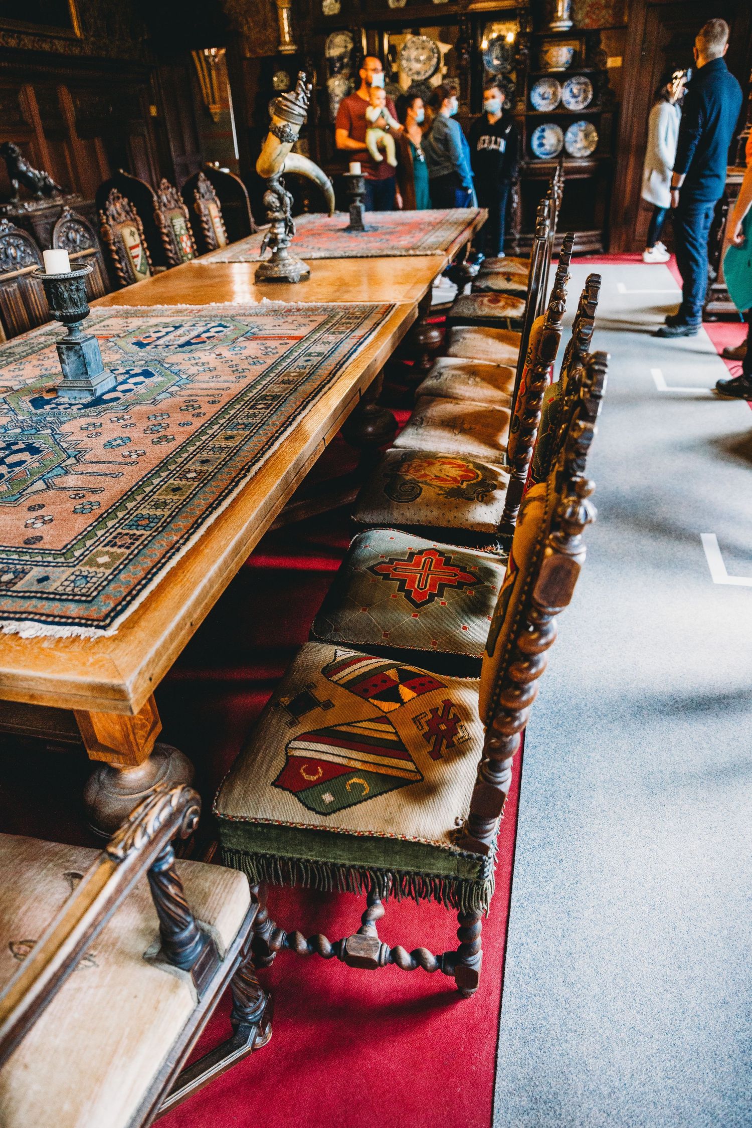 Long wooden dining table with ornate chairs and decorative carpet in medieval castle interior.