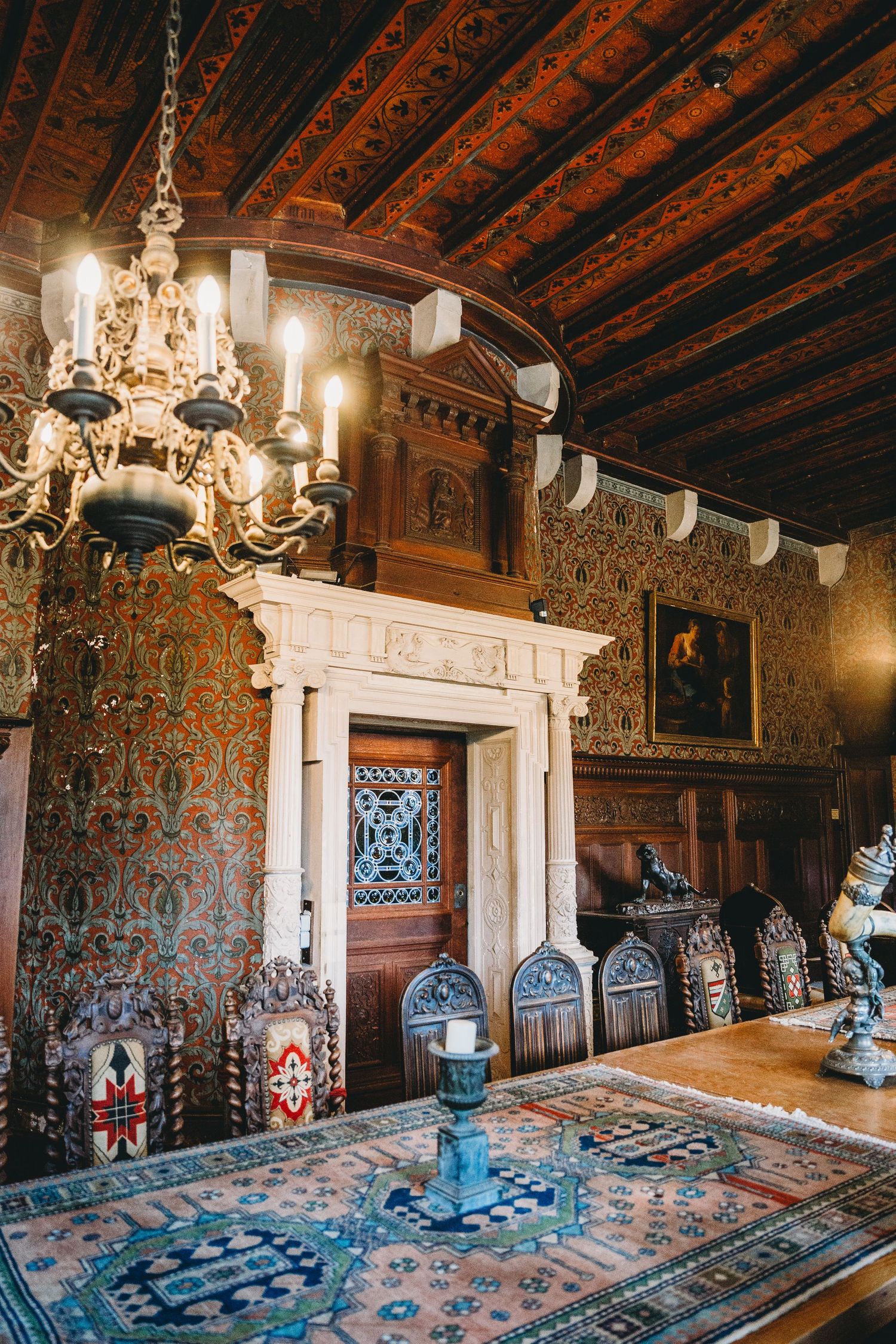 Elegant dining room with ornate chandelier, wooden ceiling and decorated walls in historic castle.
