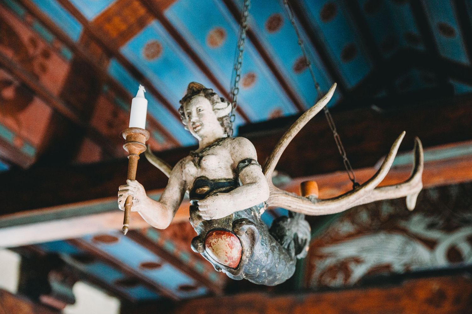 Decorative cherub statue holding a candle suspended from an ornate ceiling.
