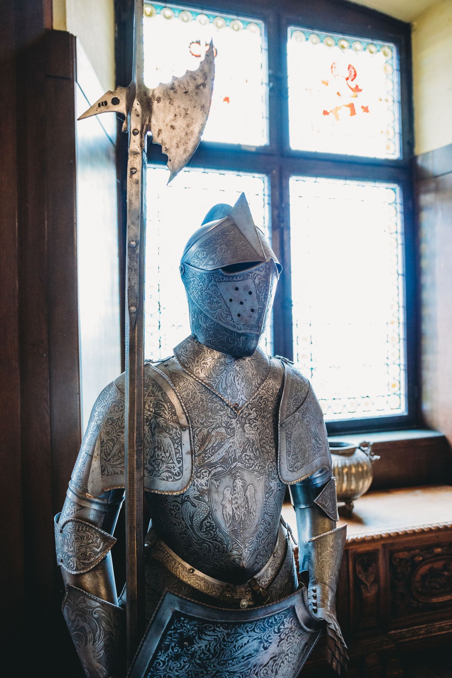 Decorative suit of armor displayed in front of stained glass windows inside castle museum.