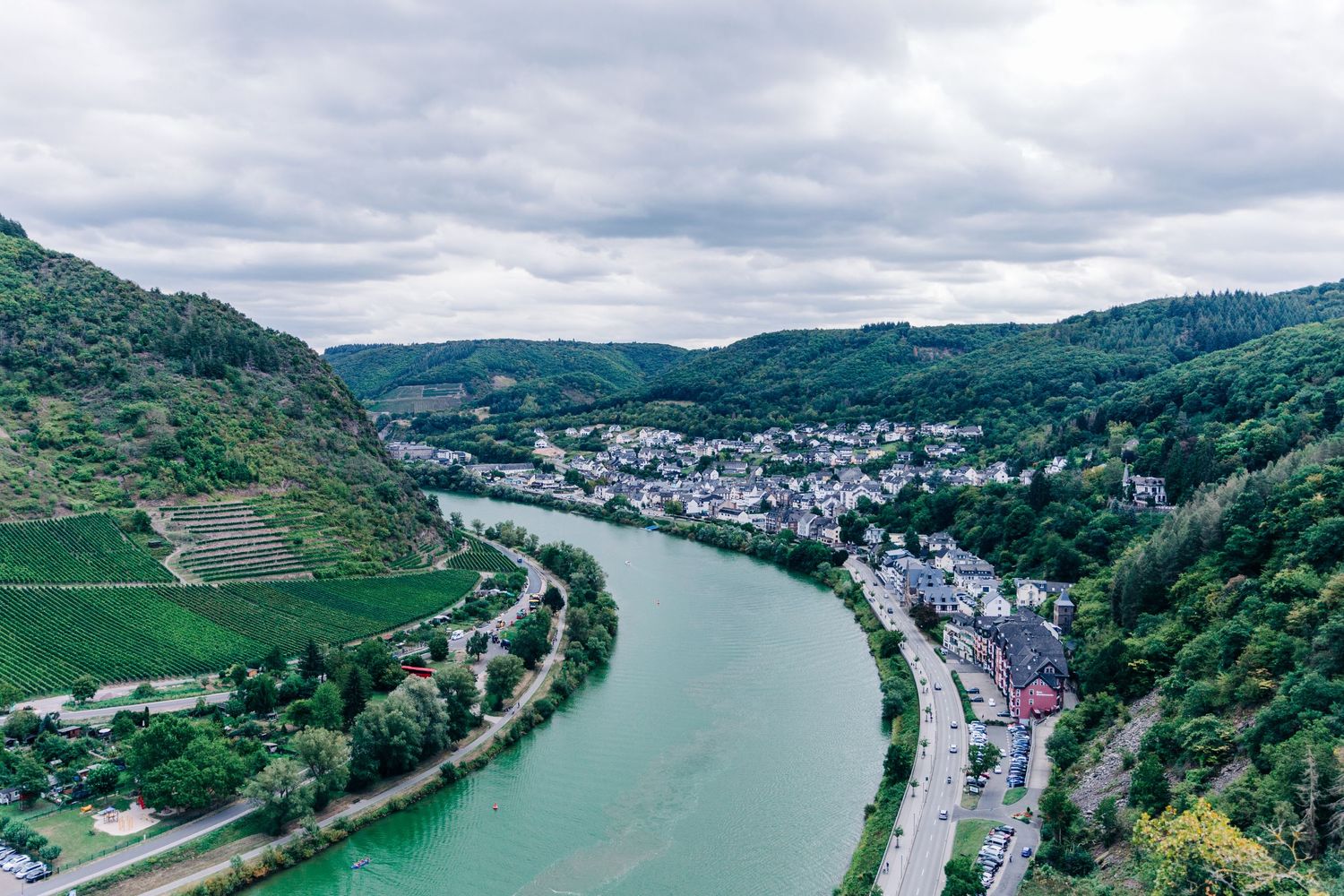 Aerial view of a winding river through green hills with terraced vineyards and a small town nestled in the valley.