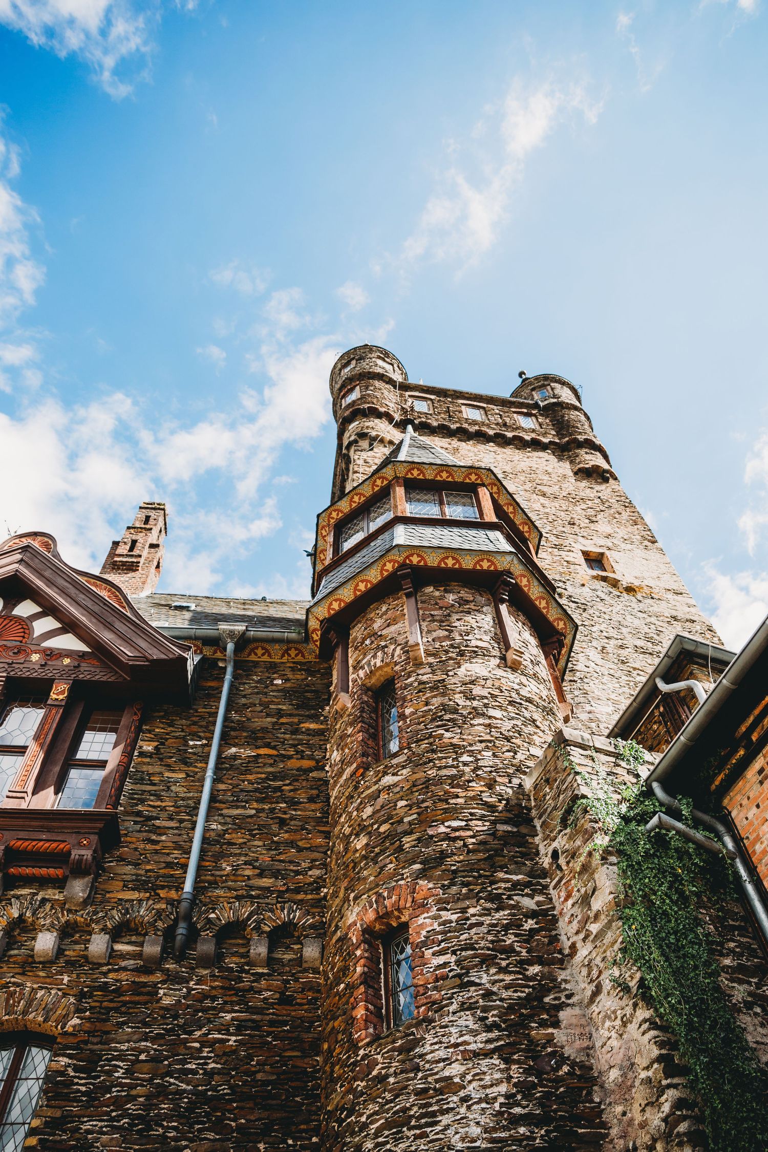 Low angle view of a medieval castle tower with stone walls and ornate architectural details against blue sky.