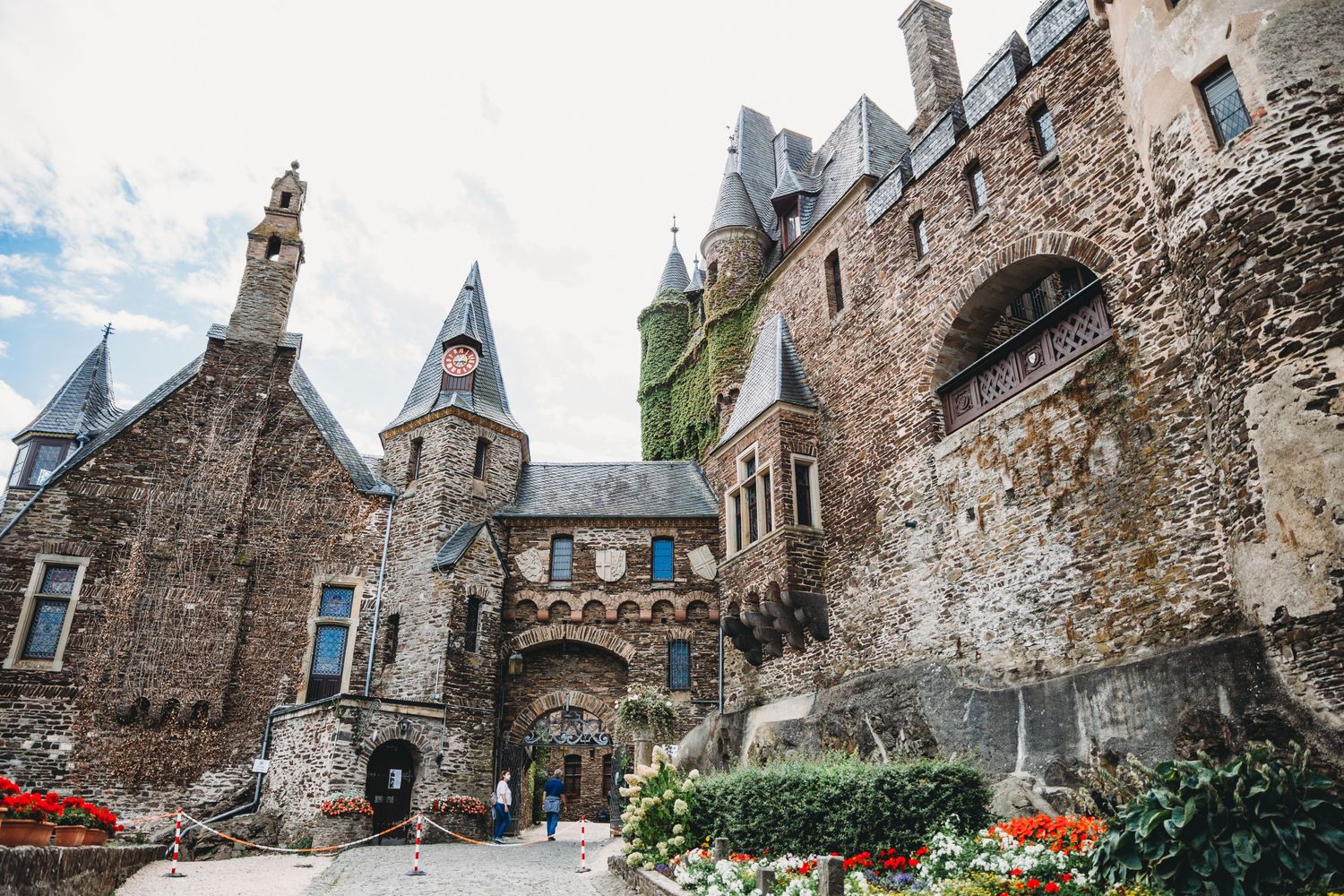 Historic castle courtyard with stone walls, medieval towers and colorful flower gardens.