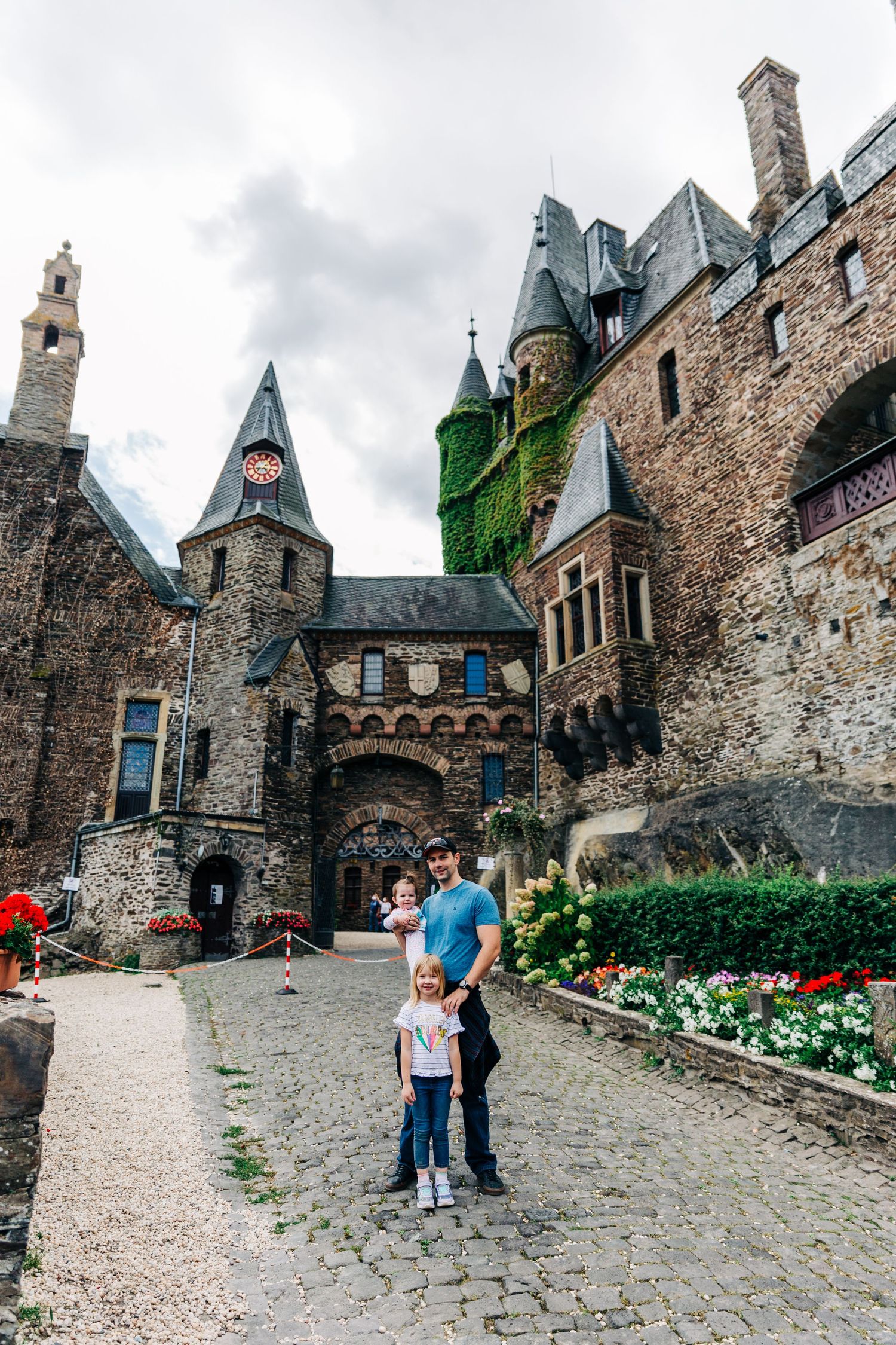 Medieval castle entrance courtyard with stone paths, towers and blooming flower gardens.
