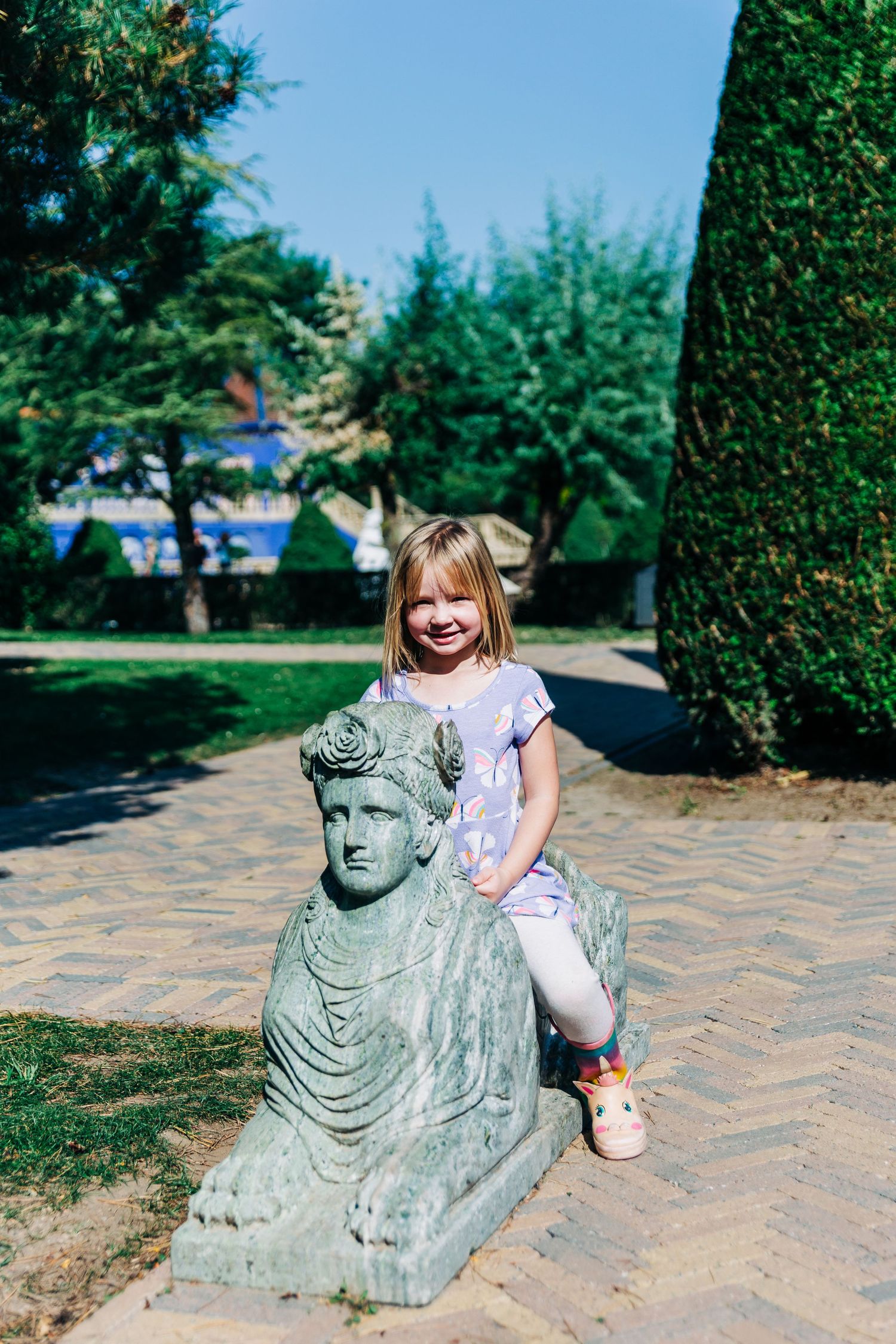 A decorative stone sphinx statue in a manicured garden setting.