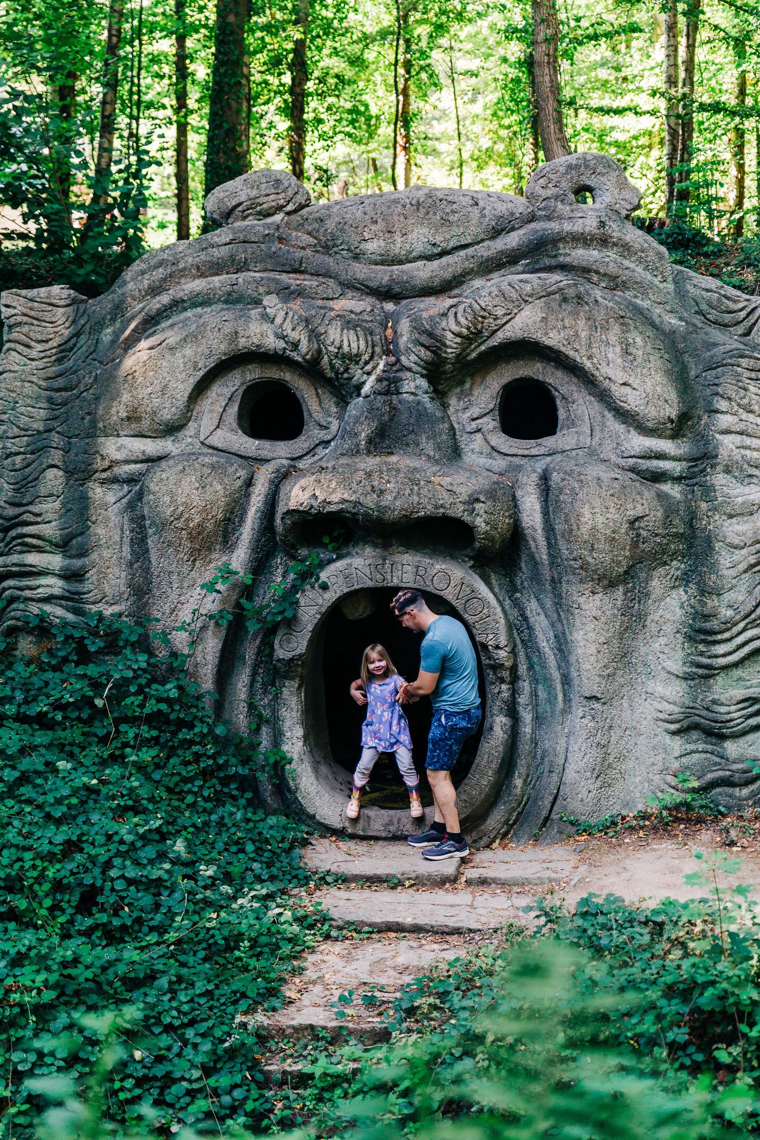 Large sculptural face carved into stone with an open mouth forming a cave entrance.