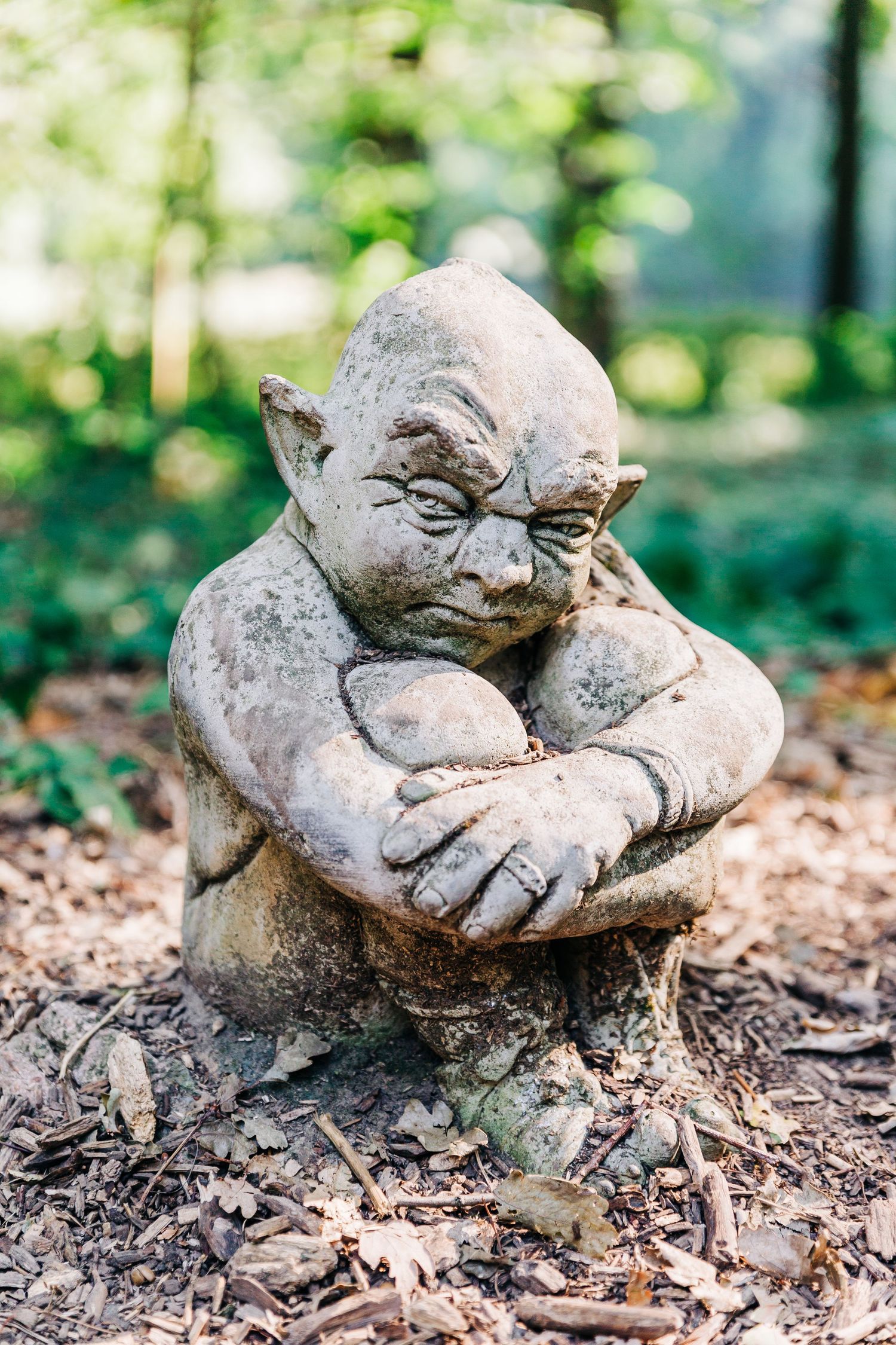 Small garden gnome statue with crossed arms made of weathered stone.