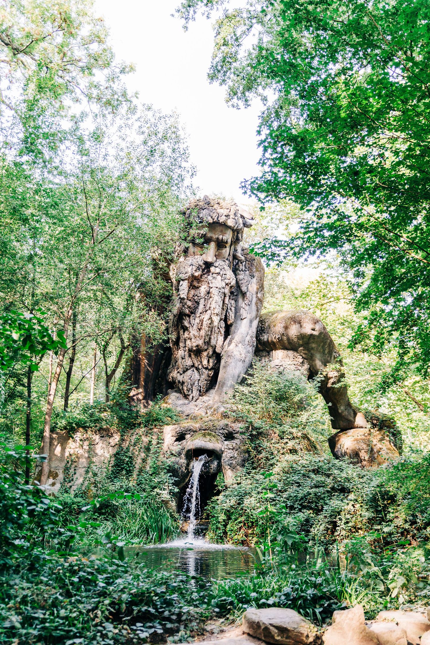 A scenic rock formation with a small waterfall in a wooded area surrounded by green trees.