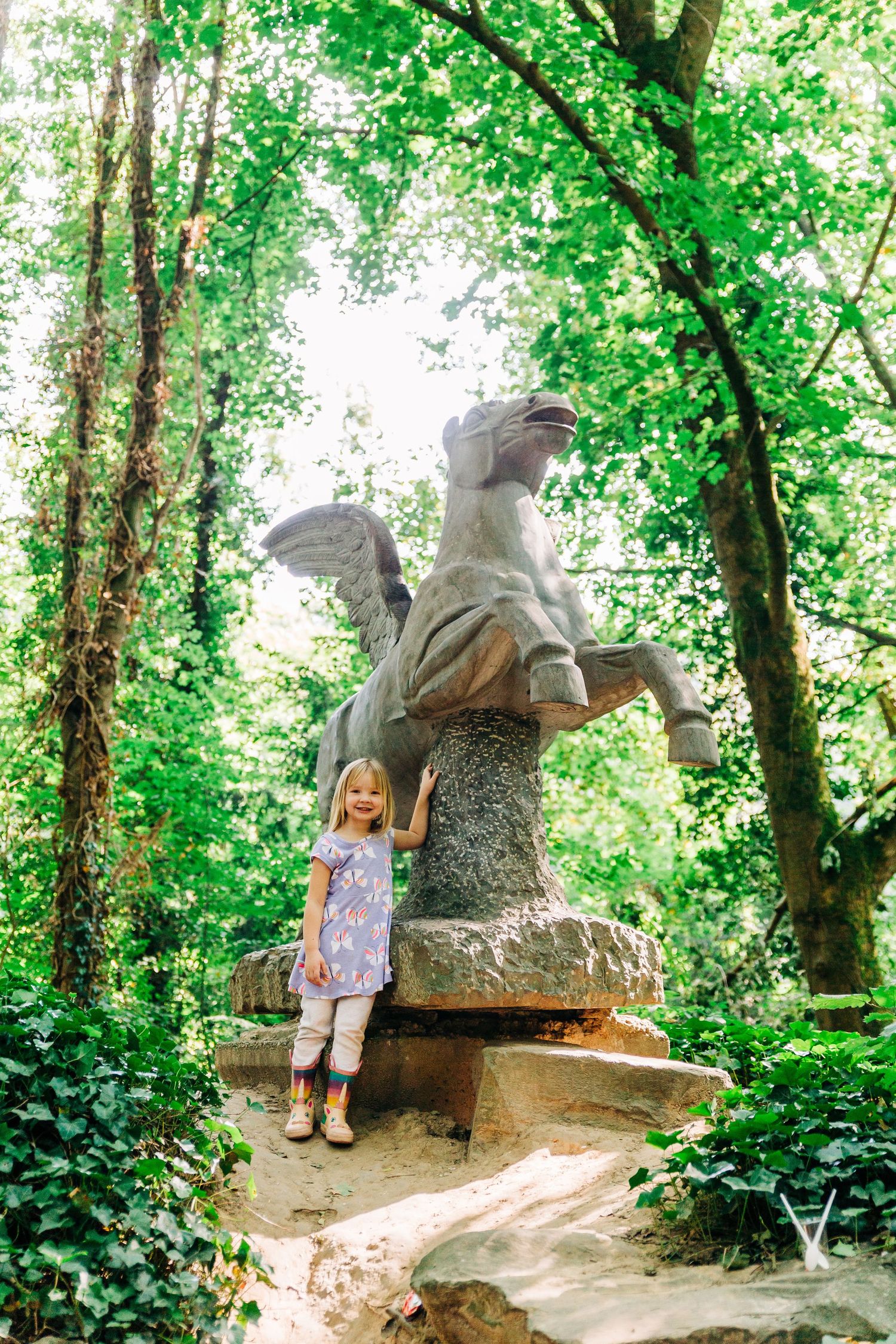 A woodland scene featuring a stone eagle statue with lush green foliage in the background.