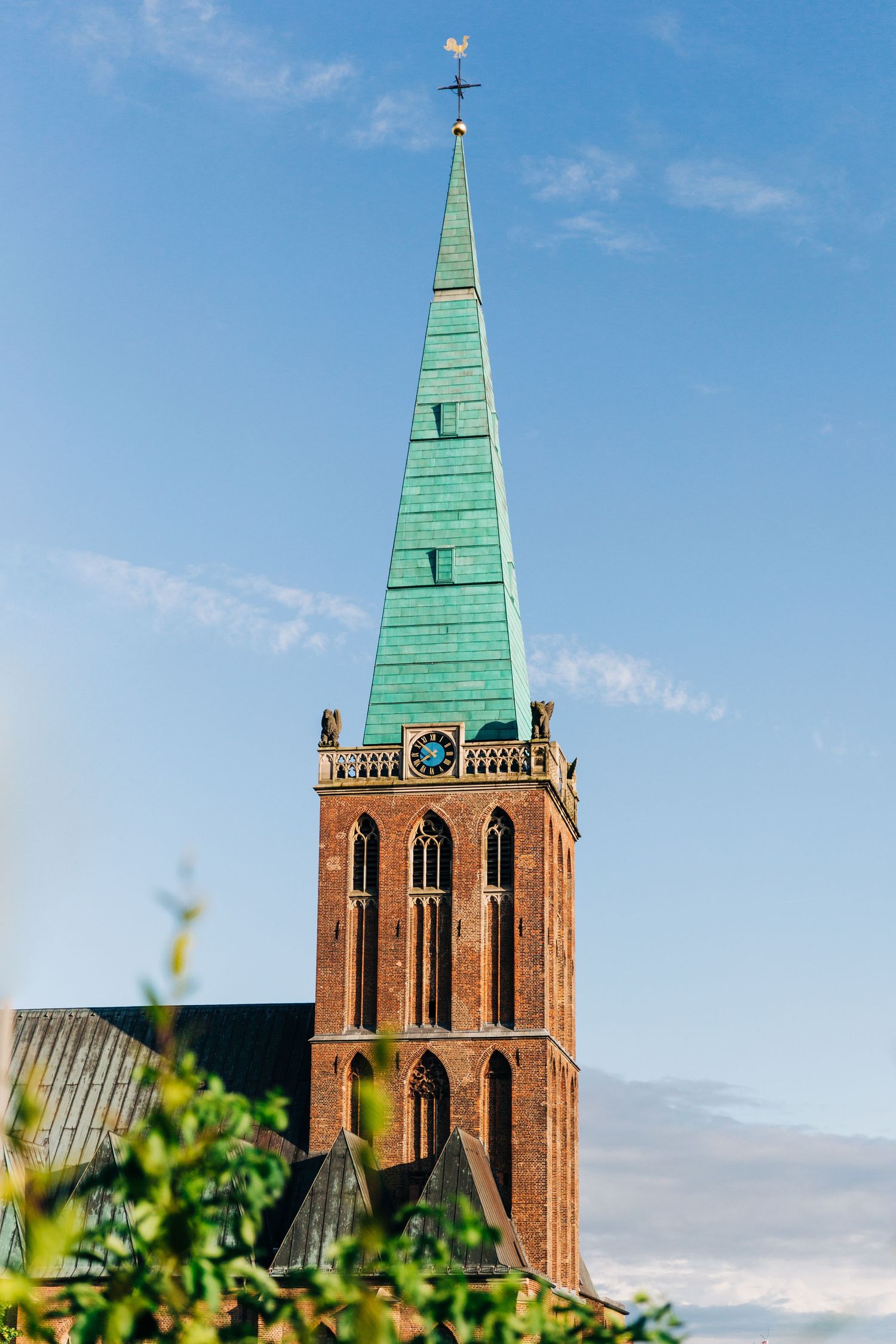 Tall church steeple with green copper spire against blue sky.