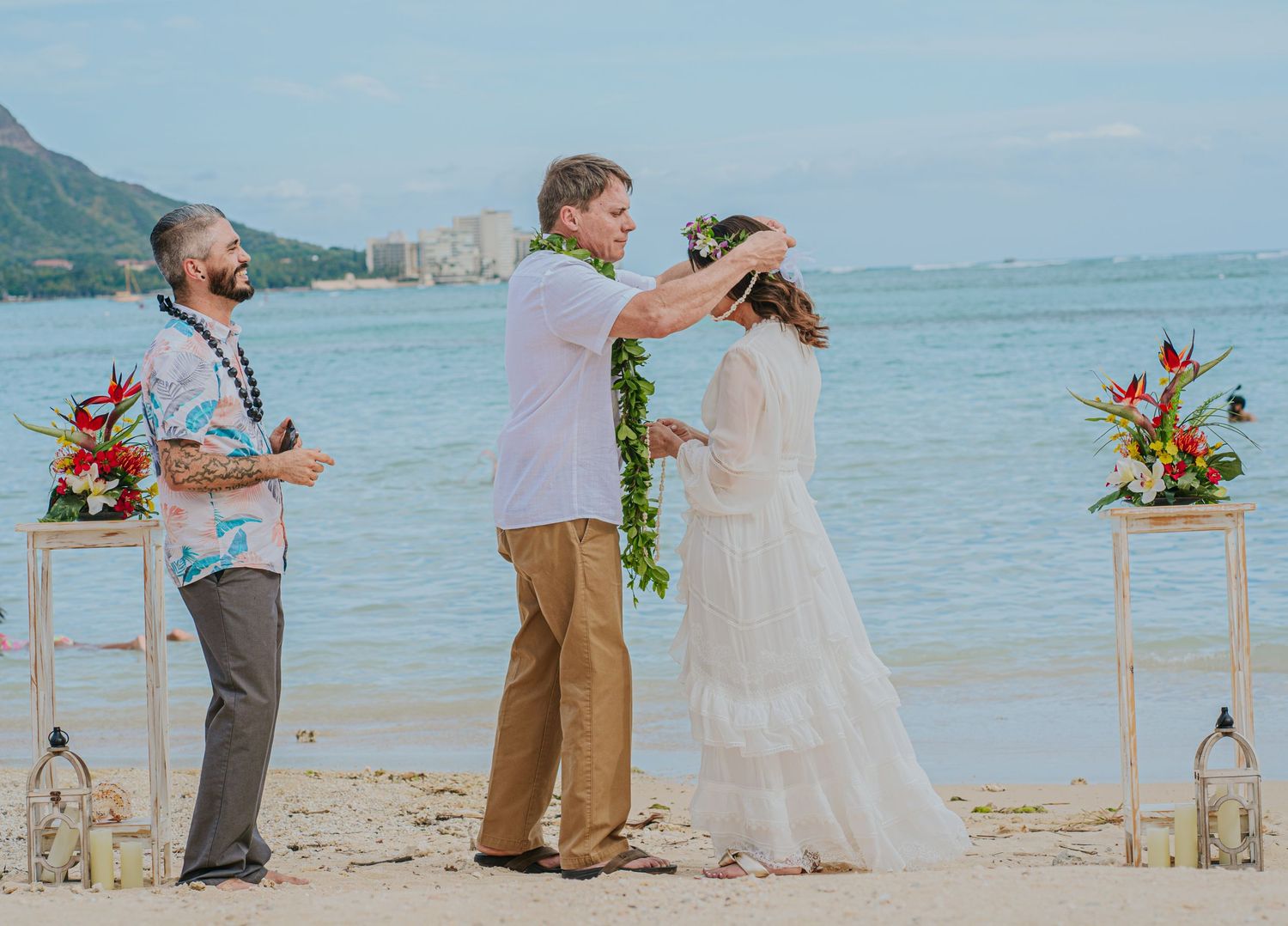 Beach wedding ceremony setup with floral arrangements and Diamond Head mountain in background.