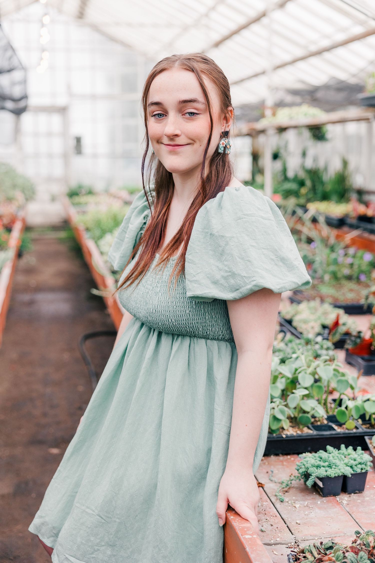 Portrait of someone in a mint dress surrounded by greenhouse plants and flowers.