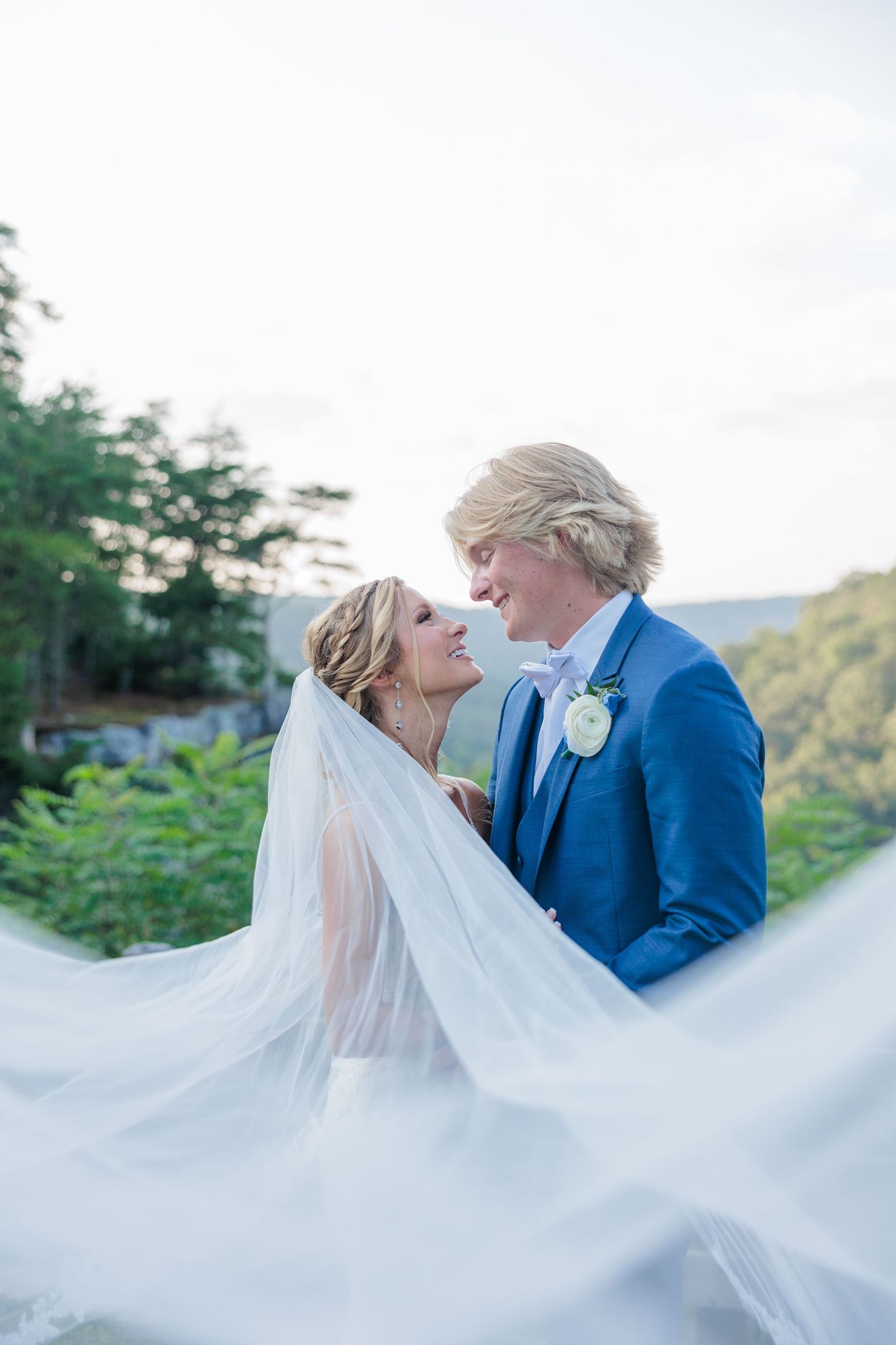 Romantic bride and groom share an intimate moment as her veil flows in the breeze against a mountain backdrop.