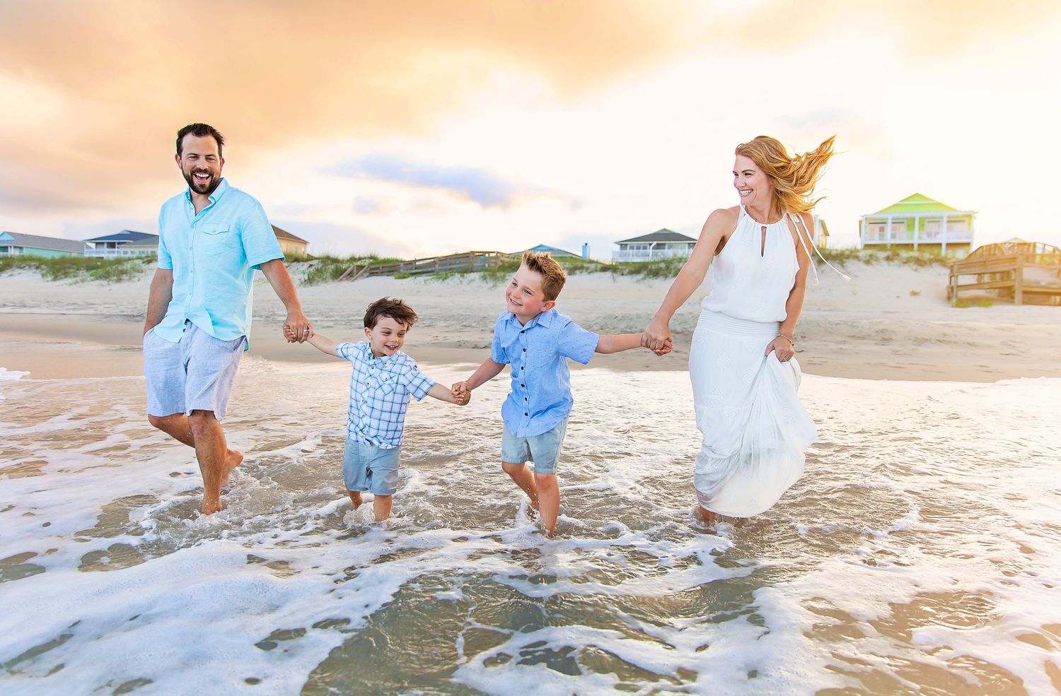 Family running and jumping together in ocean waves at beach during sunset.