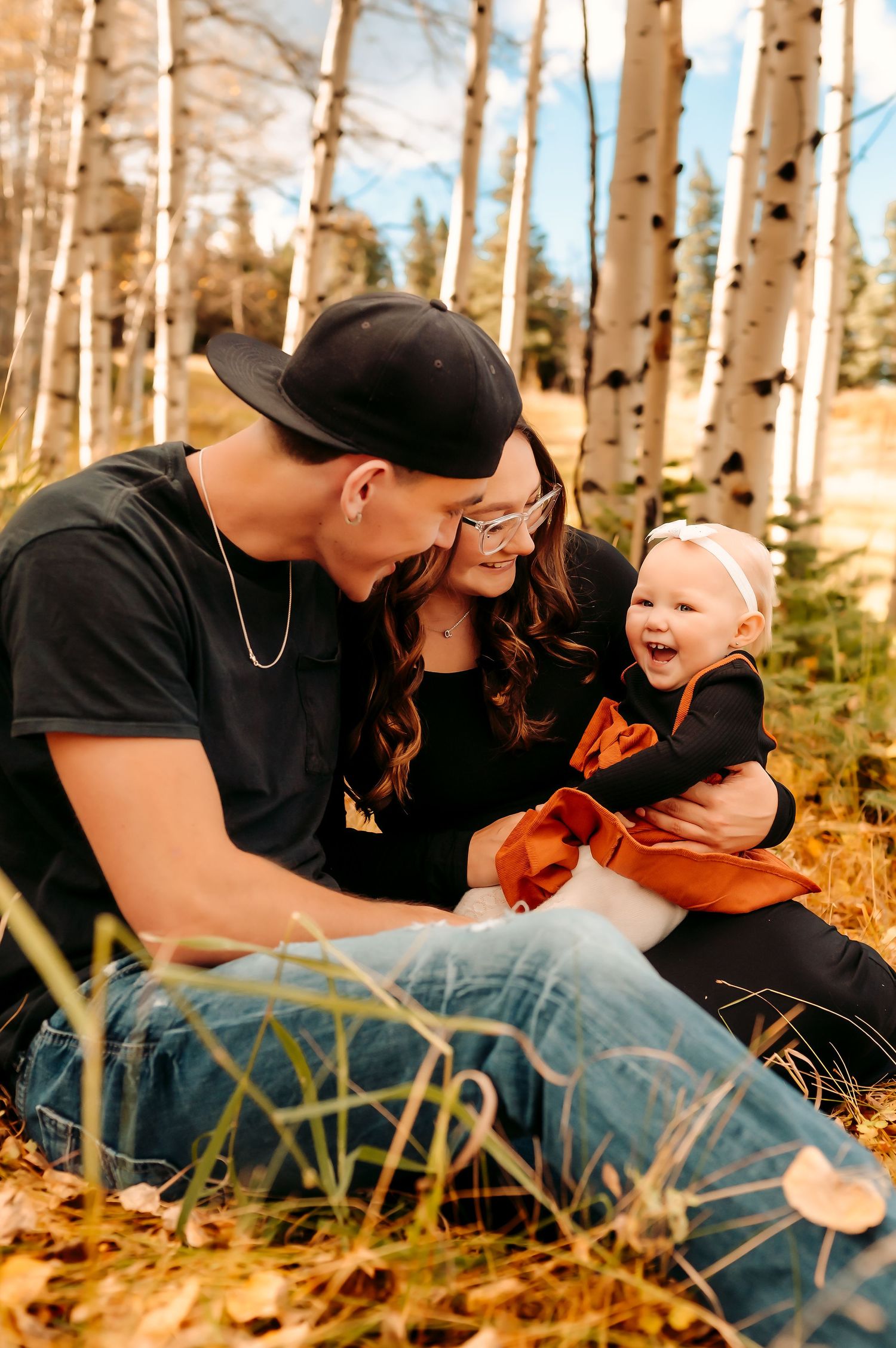 Family sitting together among fall aspen trees sharing a joyful moment.
