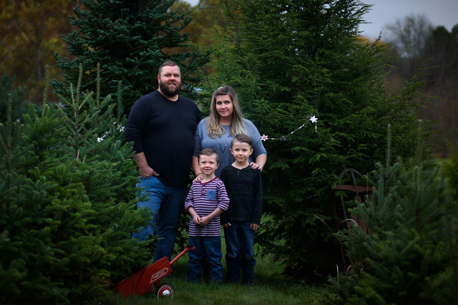Family of four posing among Christmas trees at a tree farm during the holiday season.
