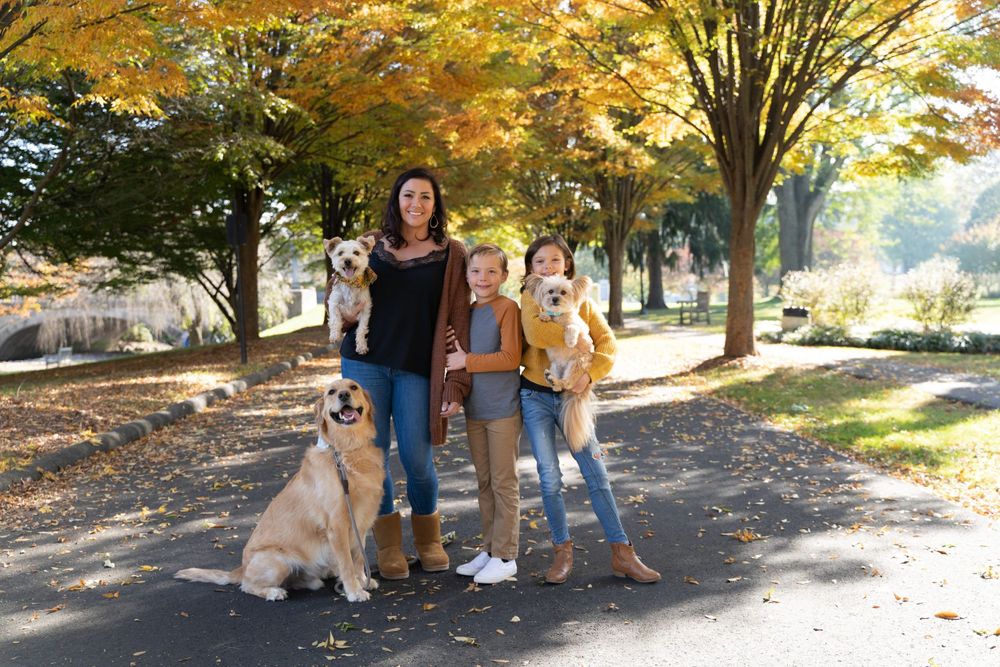 Family with children and golden retriever dog pose together under fall foliage.