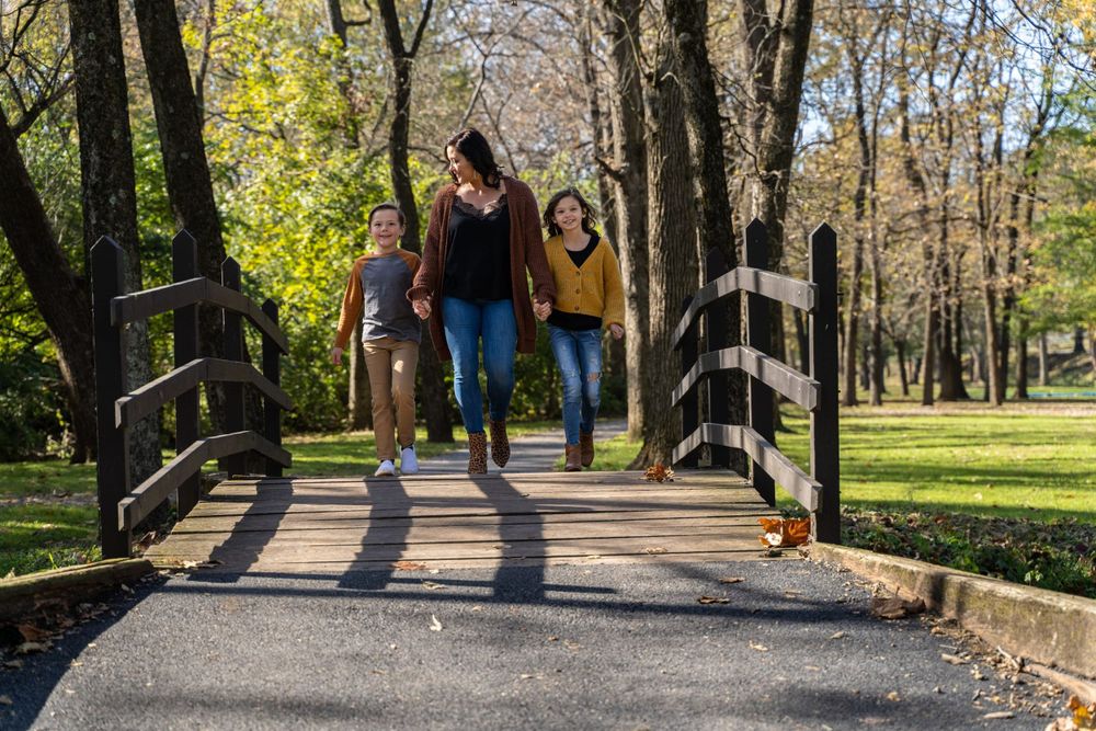 Three people walking together across a wooden bridge in a sunny autumn park.