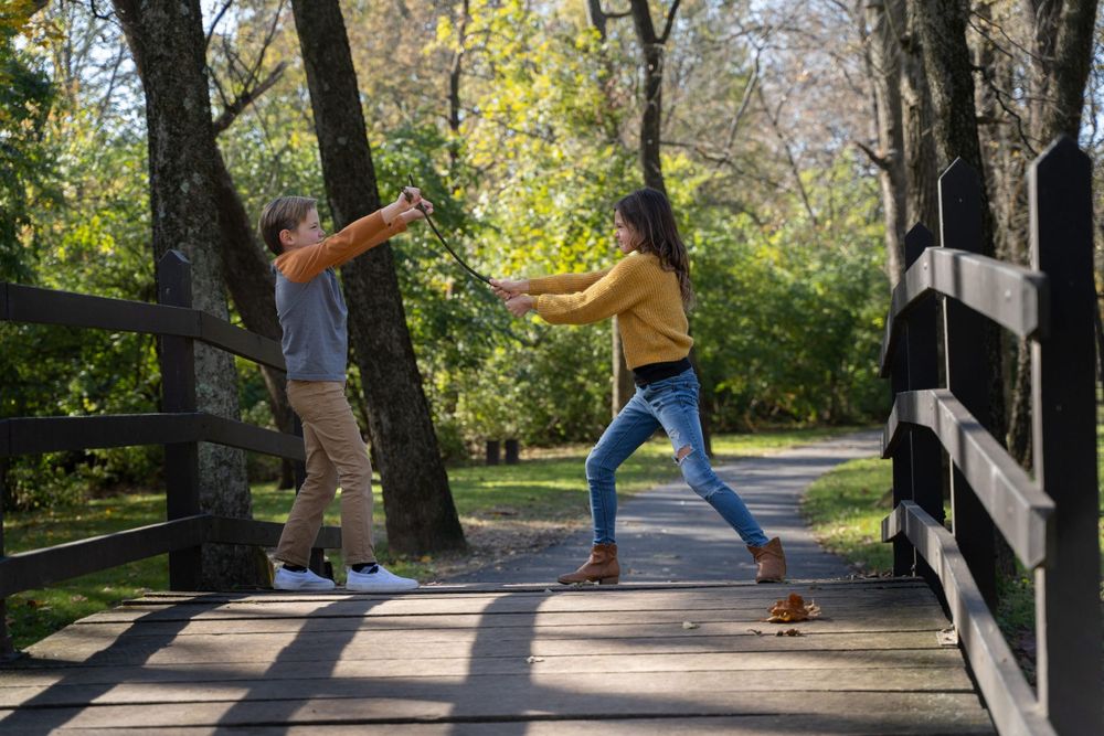 Friends playing and posing dramatically on a wooden bridge in a sunlit park.