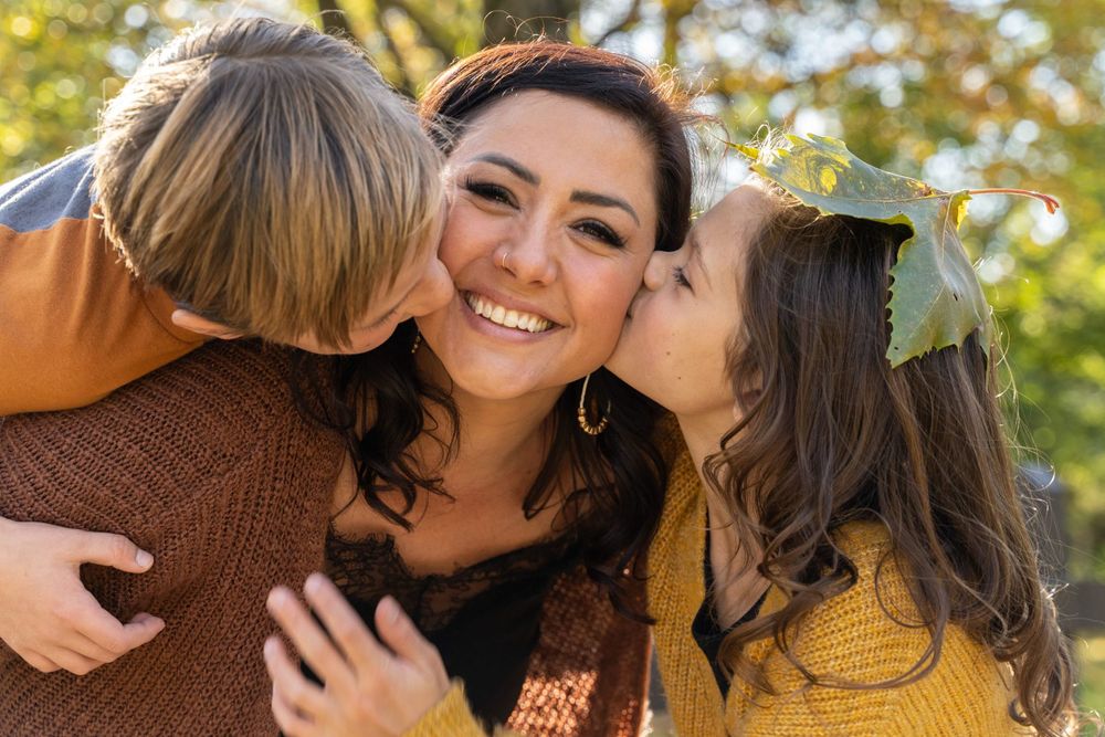A warm family moment captured outdoors with affectionate embraces in autumn sunlight.