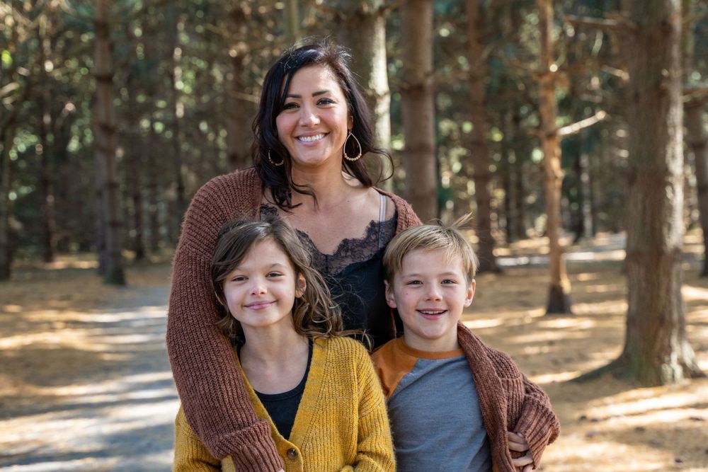 A loving family portrait captured in a sun-dappled forest setting.