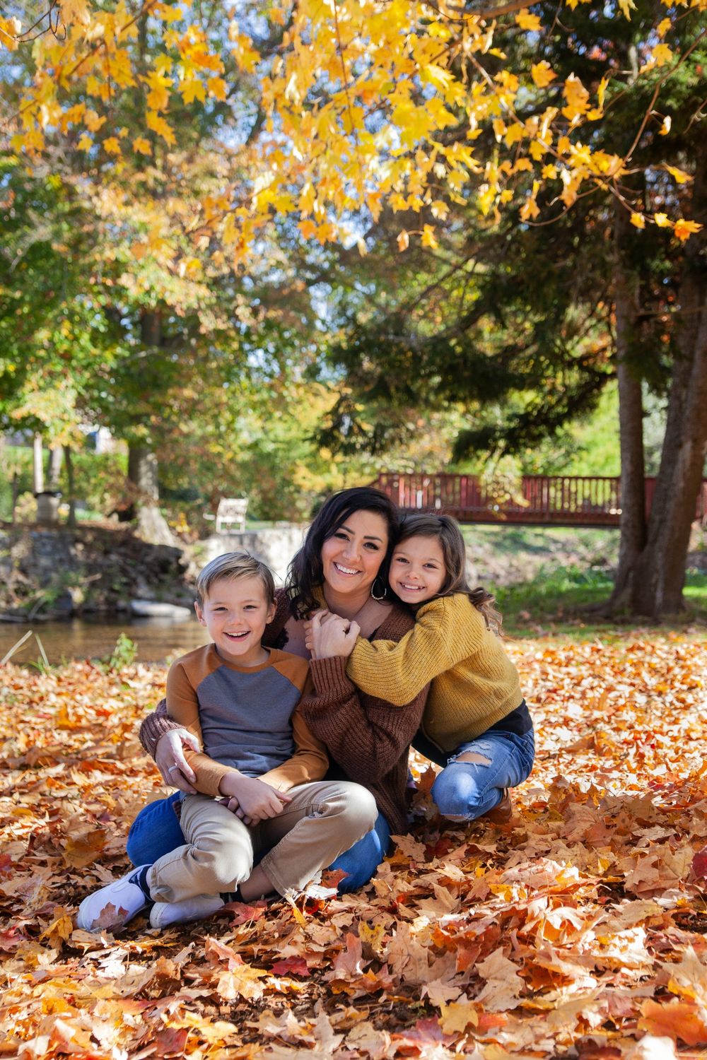 A happy autumn portrait of three people sitting together in colorful fallen leaves.