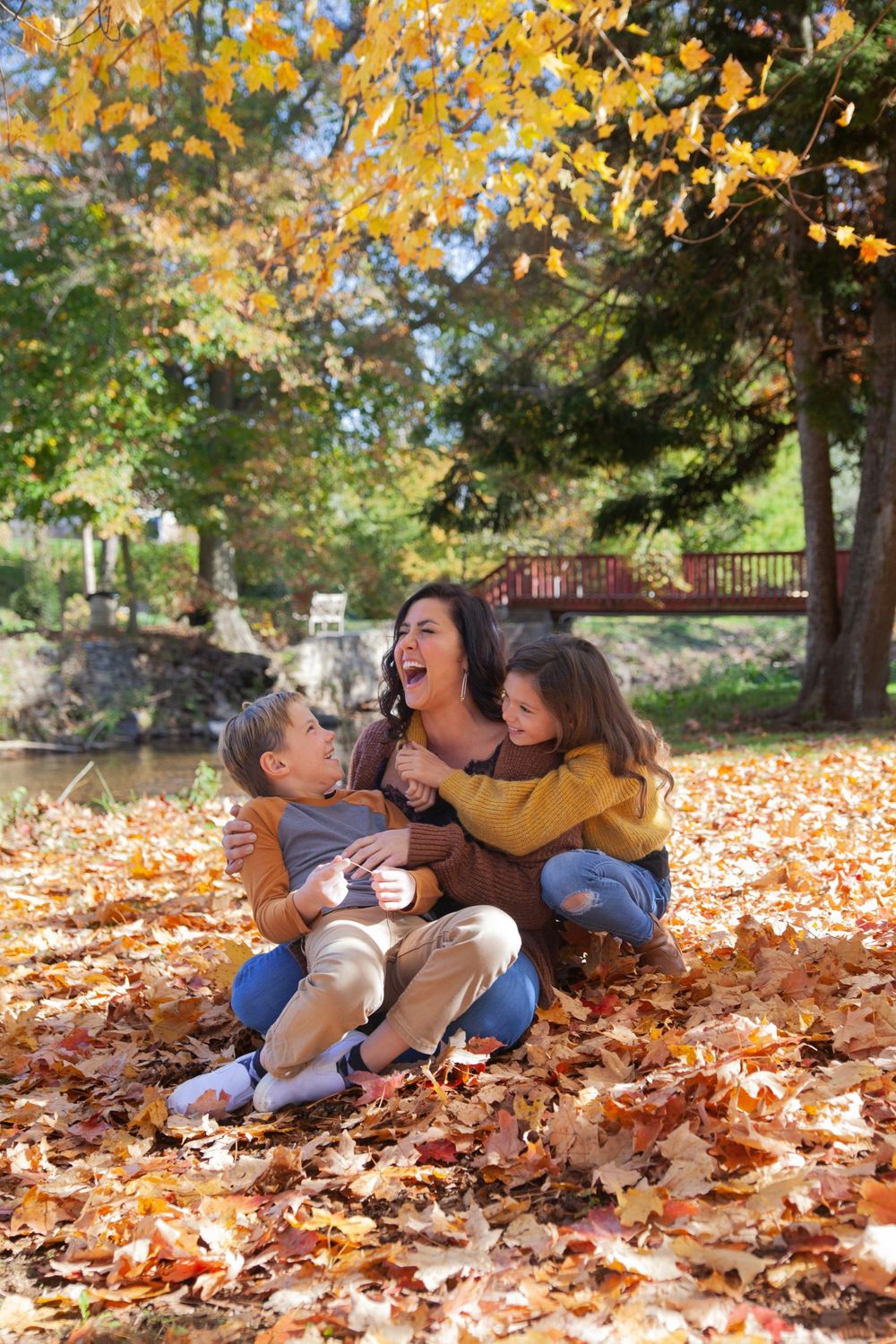 A playful autumn scene with people laughing together while sitting in fallen orange leaves.