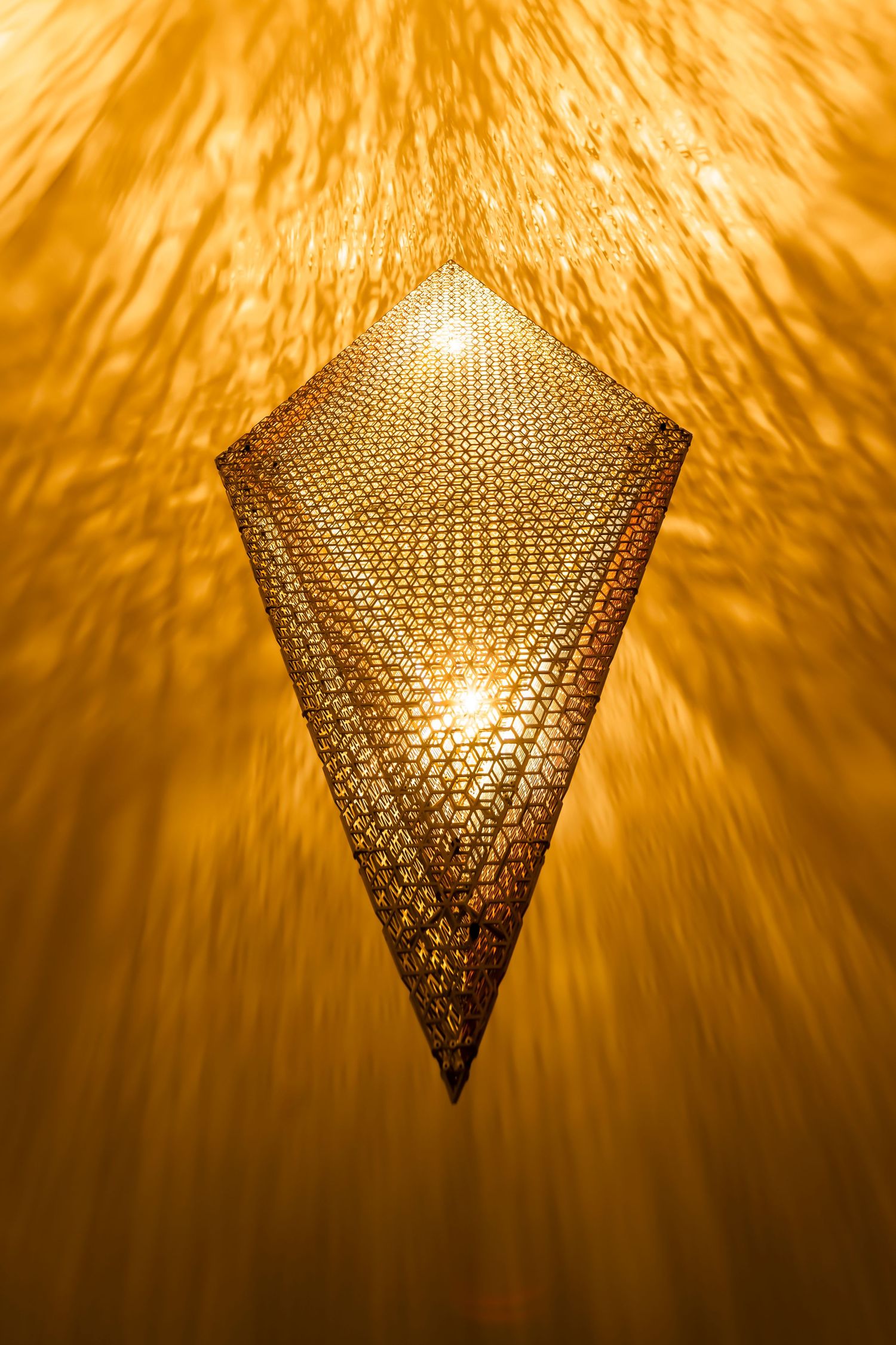 Pentagonal mesh lamp casting intricate golden light patterns in darkness.